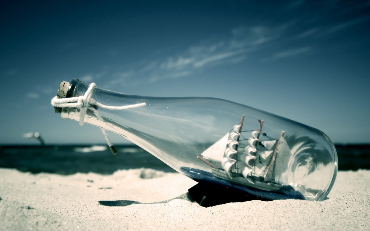 Ship in a bottle on a sandy beach HD Wallpaper