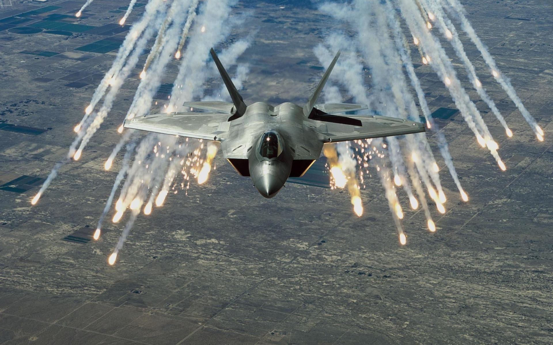 F-22 Raptor releasing flares over a landscape HD Wallpaper