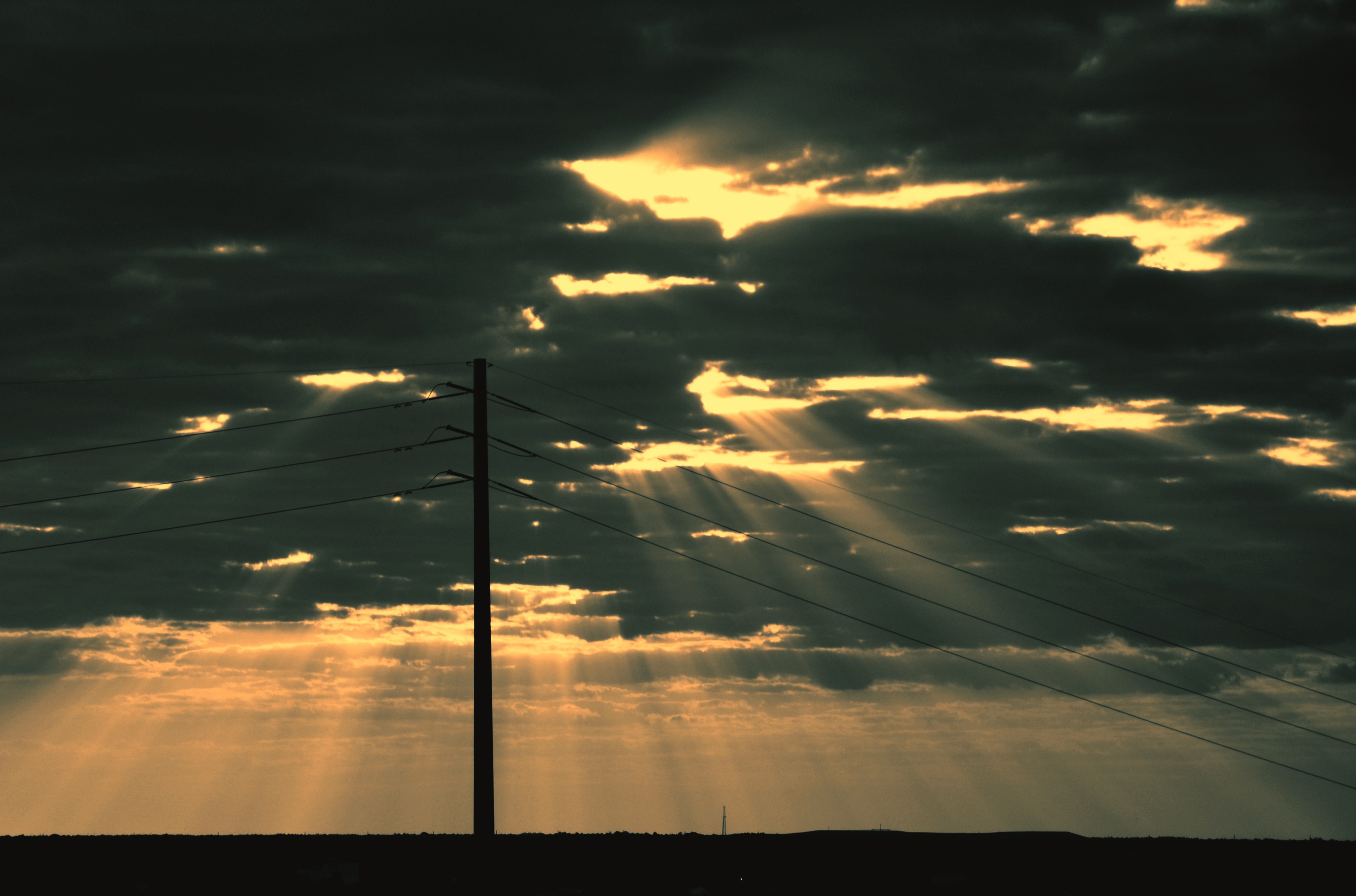 Sun rays breaking through dark clouds over a silhouette horizon HD Wallpaper