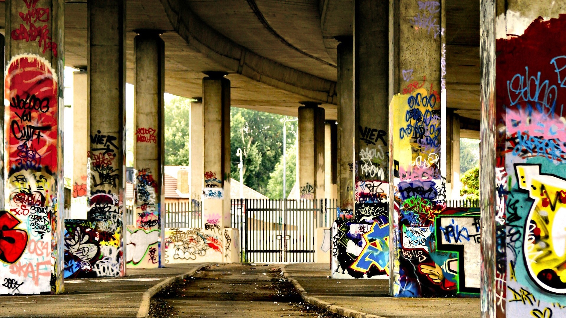 Graffiti-covered pillars under a concrete overpass HD Wallpaper