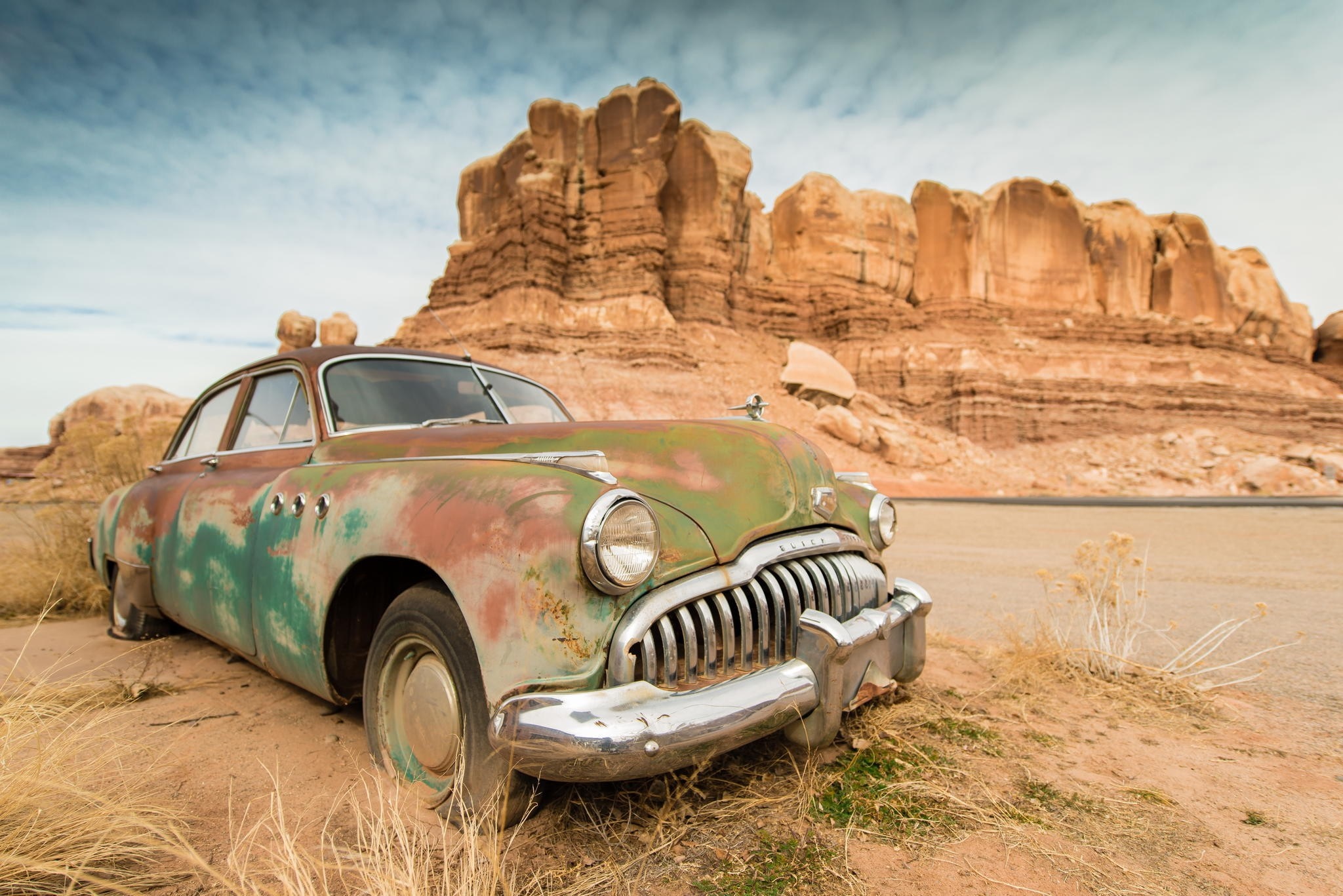 Rusted vintage car in a desert landscape with rock formations HD Wallpaper