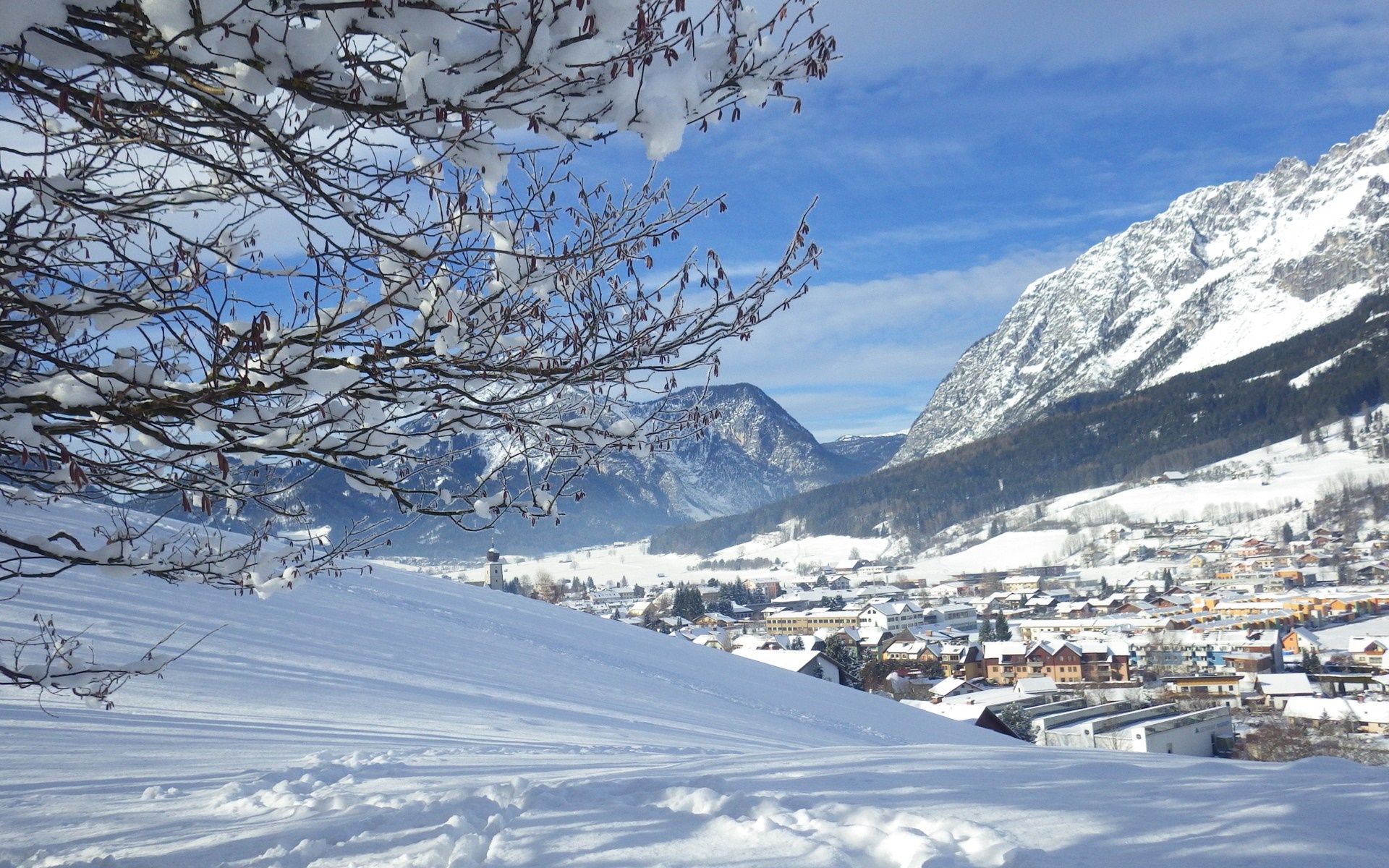 Snowy village nestled in the Alps with snow-covered mountains HD Wallpaper