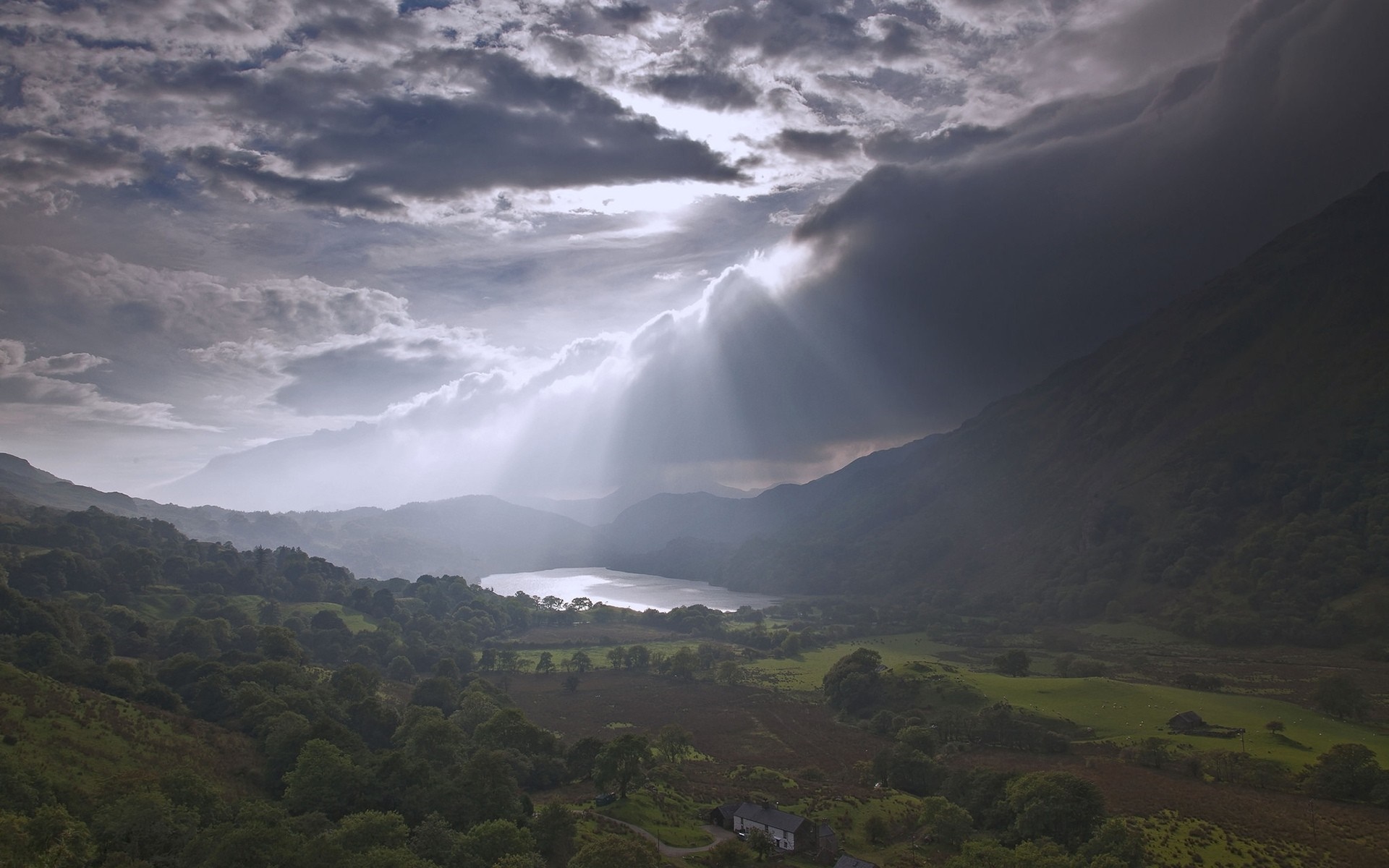 Sunlight breaking through clouds over a valley with a loch HD Wallpaper