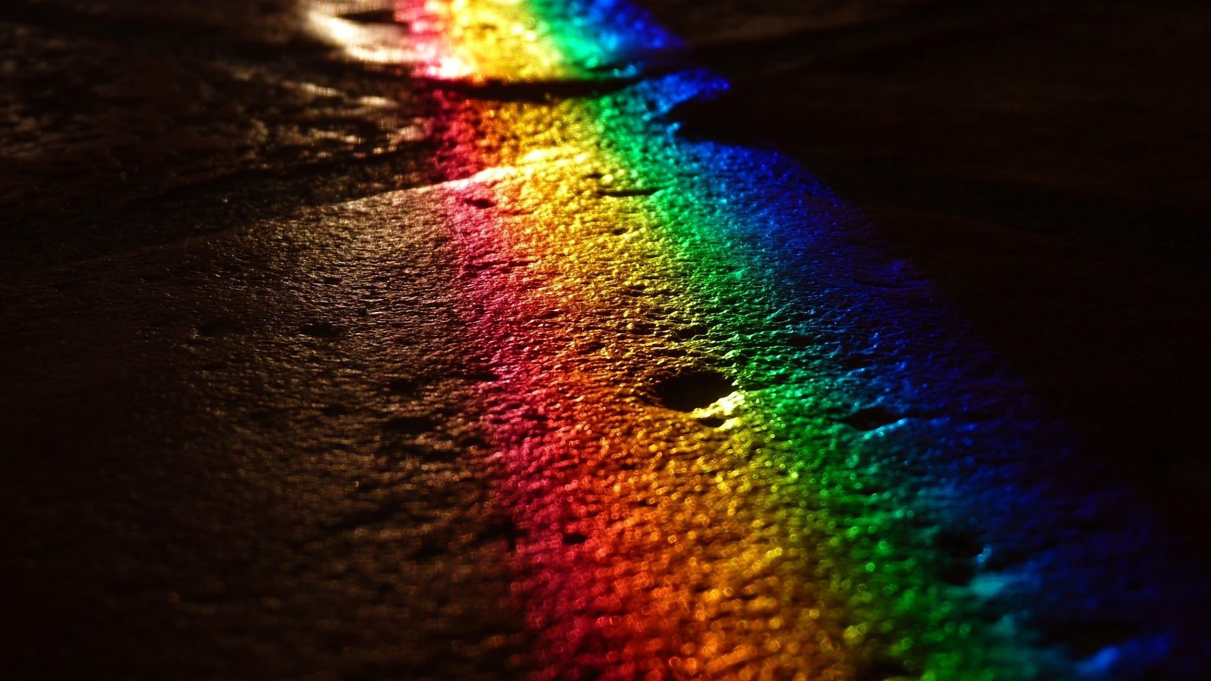 Rainbow light reflection on wet dark surface HD Wallpaper