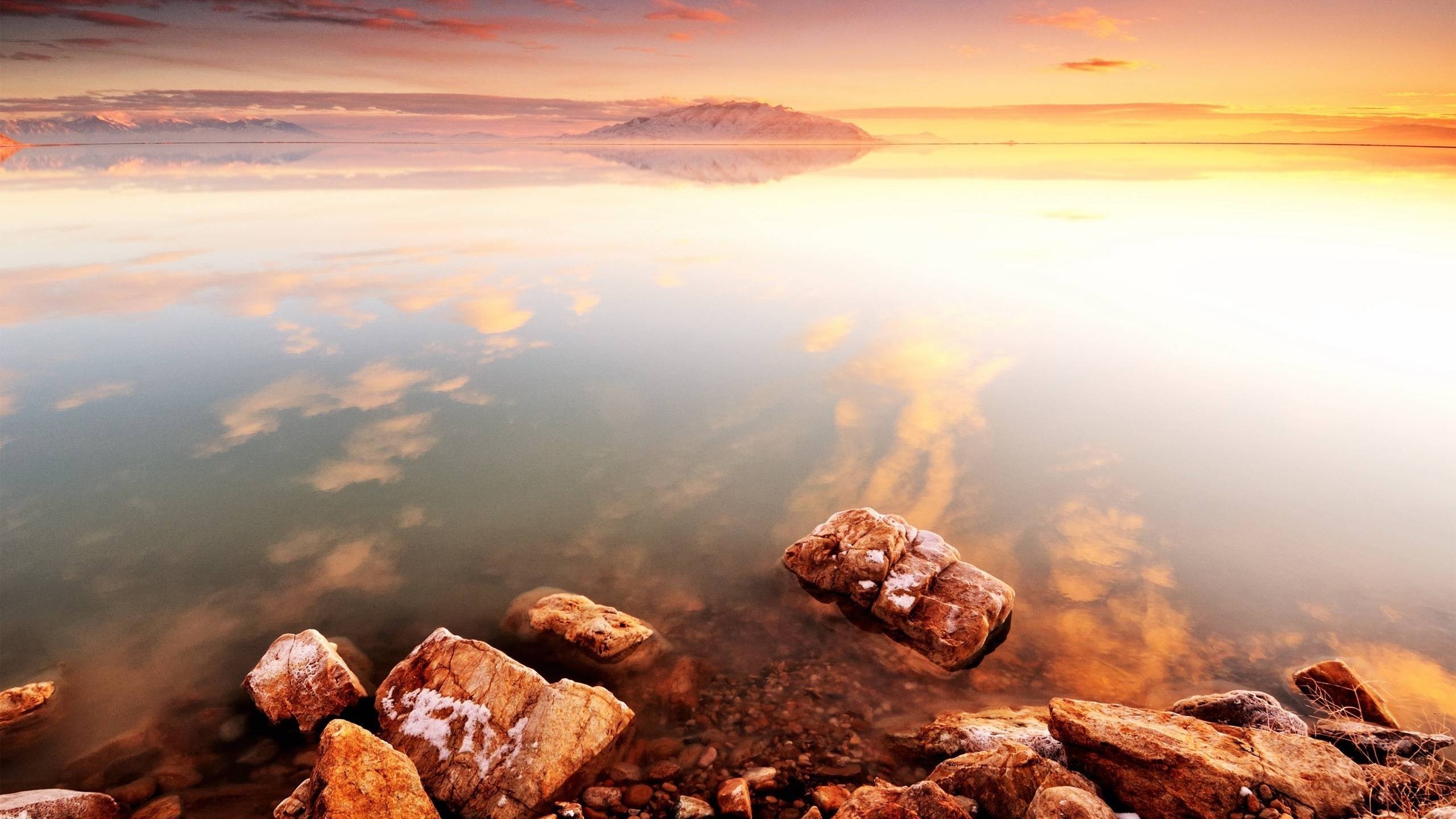 Sunset reflection over a calm body of water with rocks HD Wallpaper