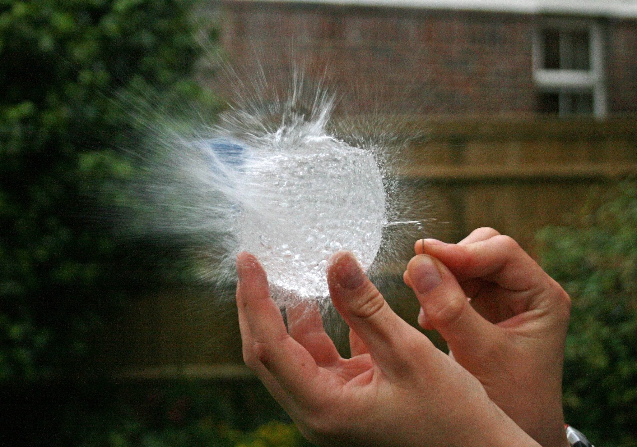 Hands bursting a water balloon with a pin HD Wallpaper