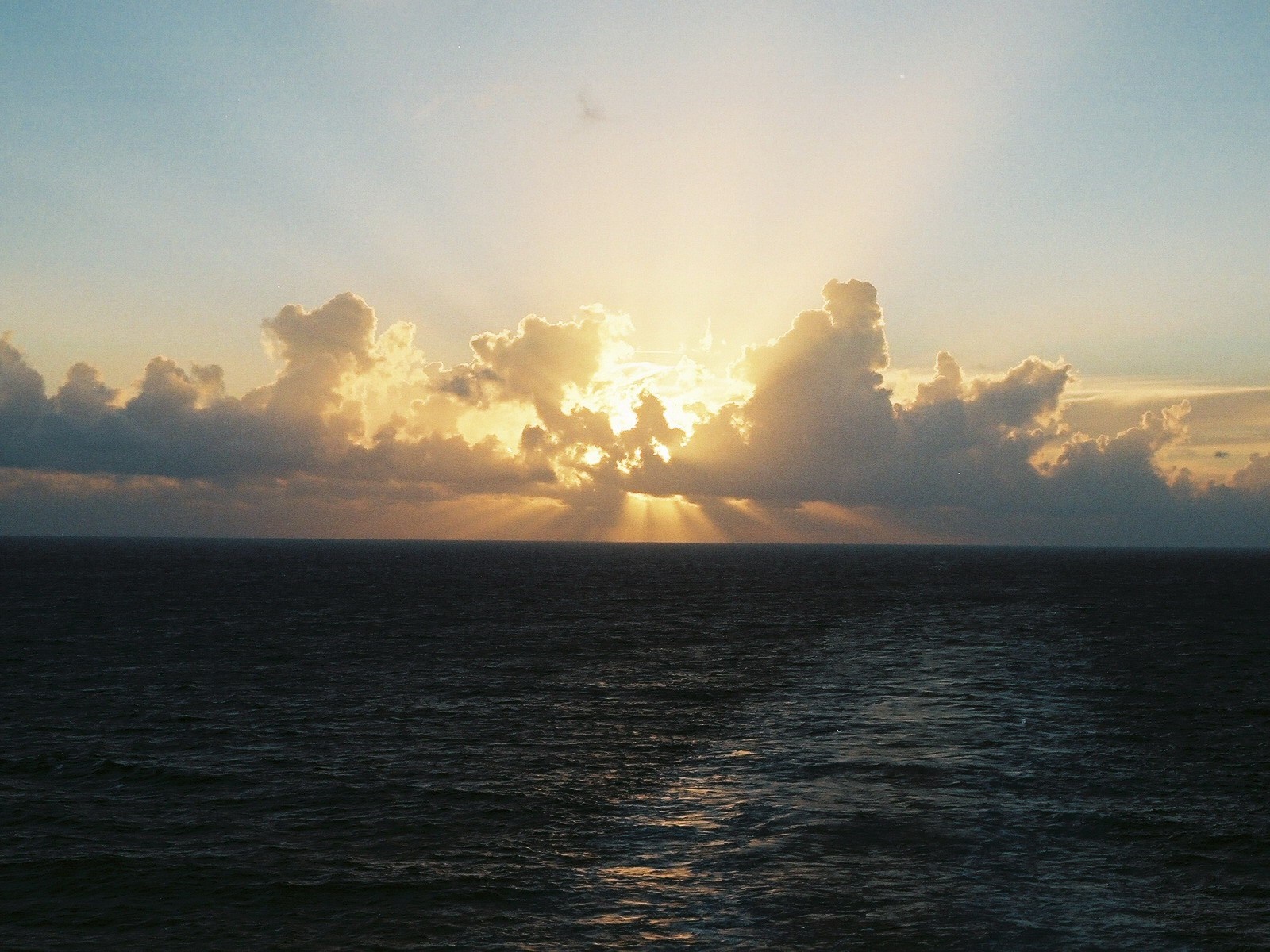 Sunlight breaking through clouds over the ocean at sunset HD Wallpaper