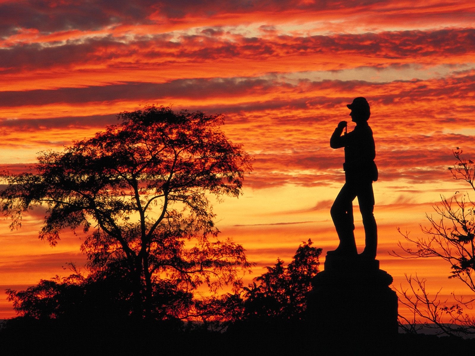 Silhouette of a soldier statue against a sunset sky HD Wallpaper