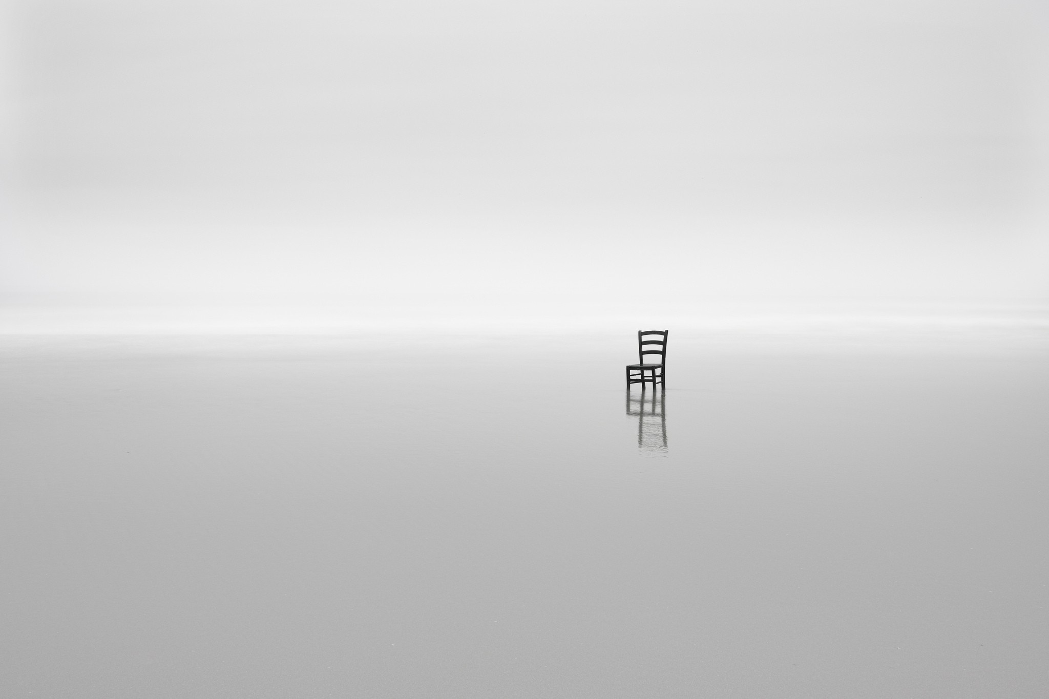 Minimalist black chair on a reflective surface with a white horizon HD Wallpaper