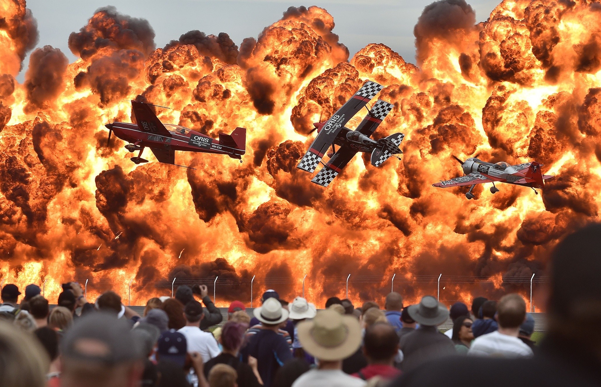 Airplanes flying through a large explosion with a crowd watching HD Wallpaper