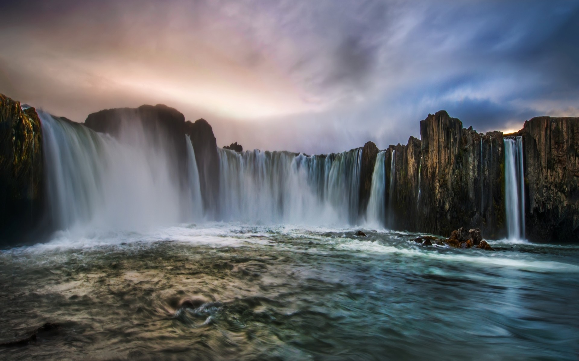 Waterfall cascading over rocks into a body of water HD Wallpaper