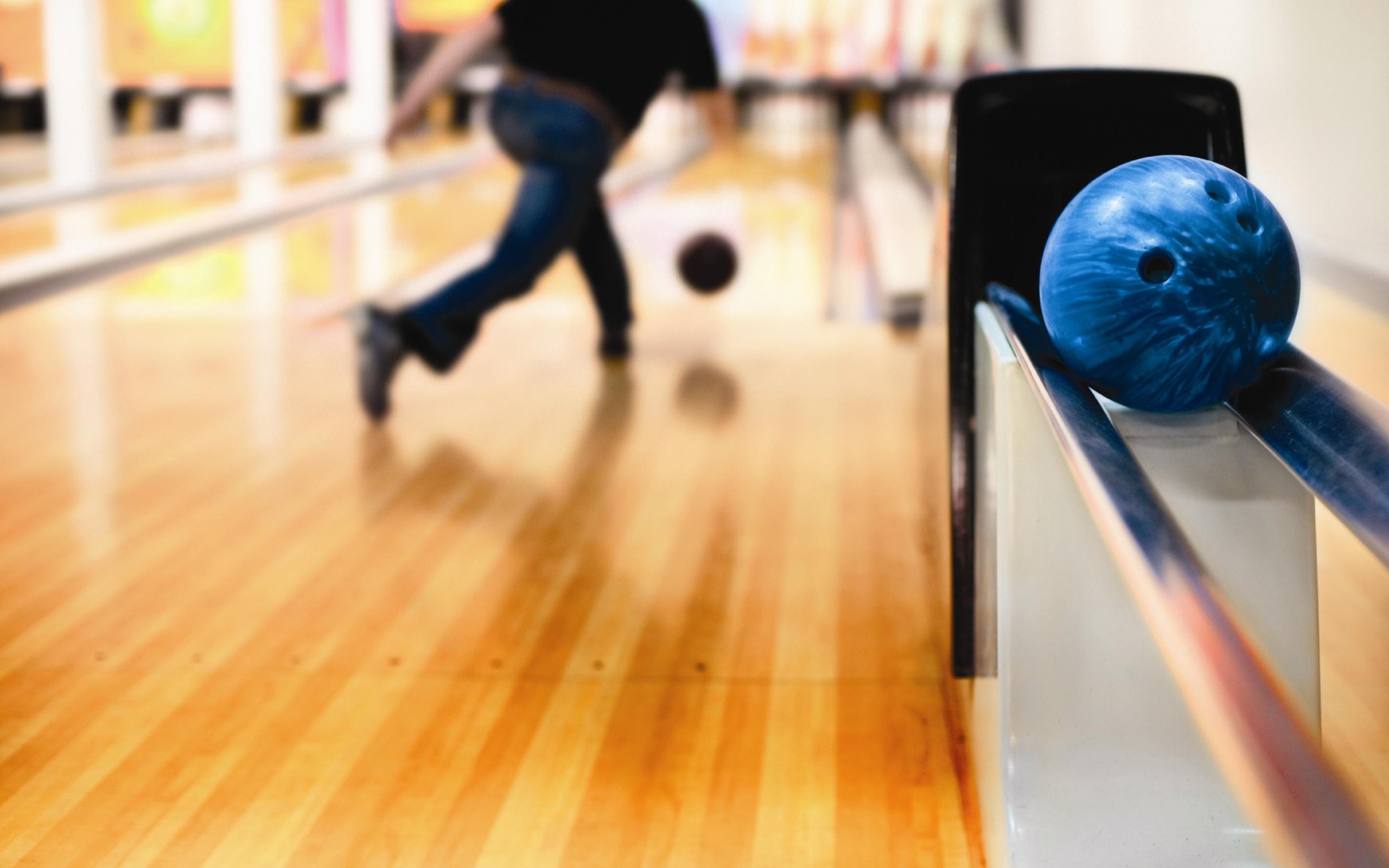 Bowling ball on a lane with a bowler in the background HD Wallpaper