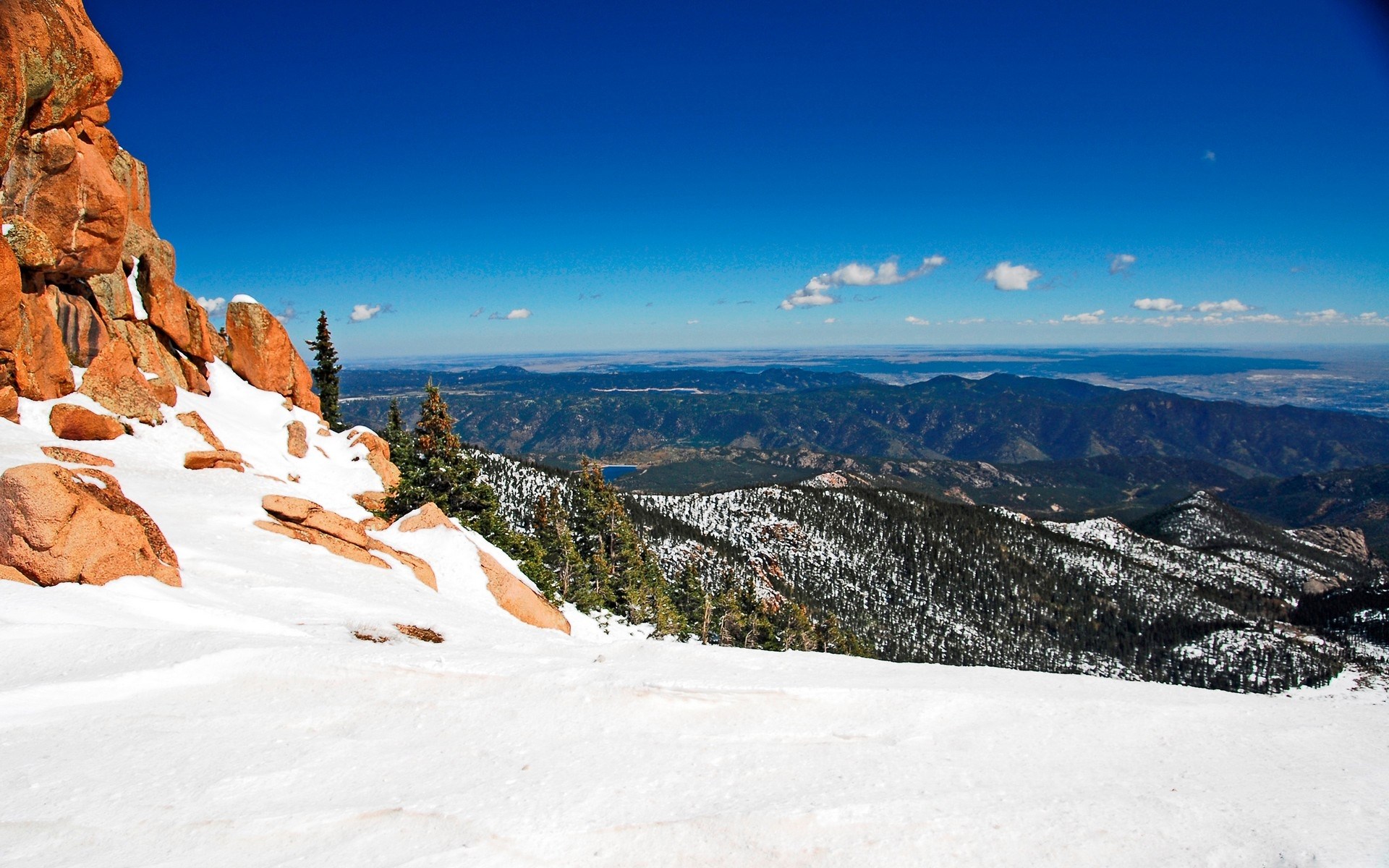 Snowy mountain landscape with rocky outcrops and distant mountains HD Wallpaper