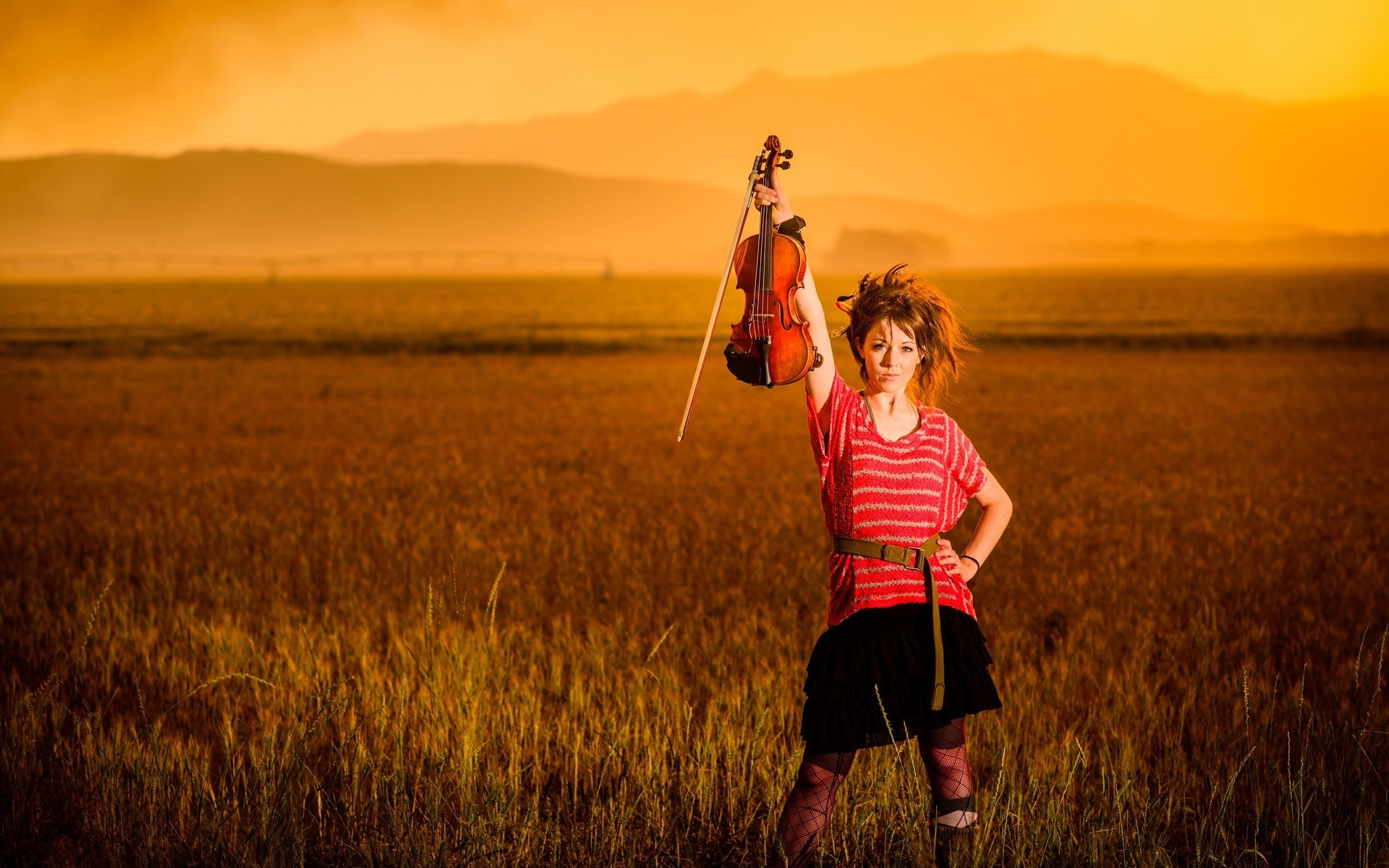 Woman holding a violin in a field at sunset HD Wallpaper