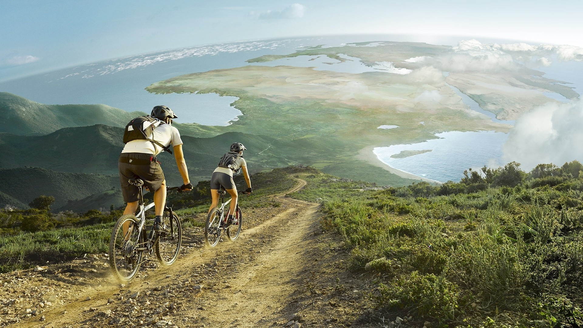 Two people mountain biking on a dirt road with a panoramic view HD Wallpaper