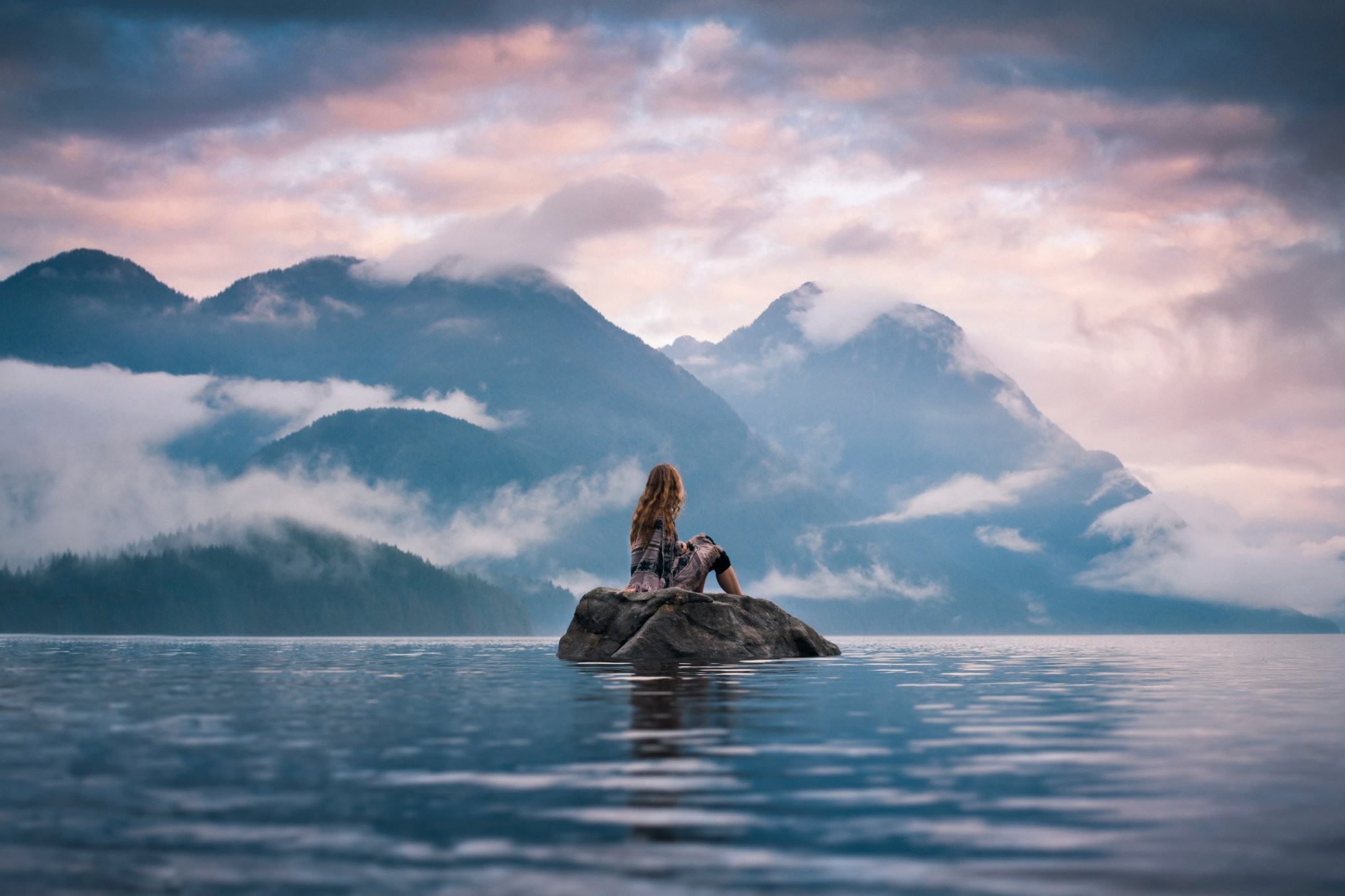 Woman sitting on a rock in a lake with mountains HD Wallpaper
