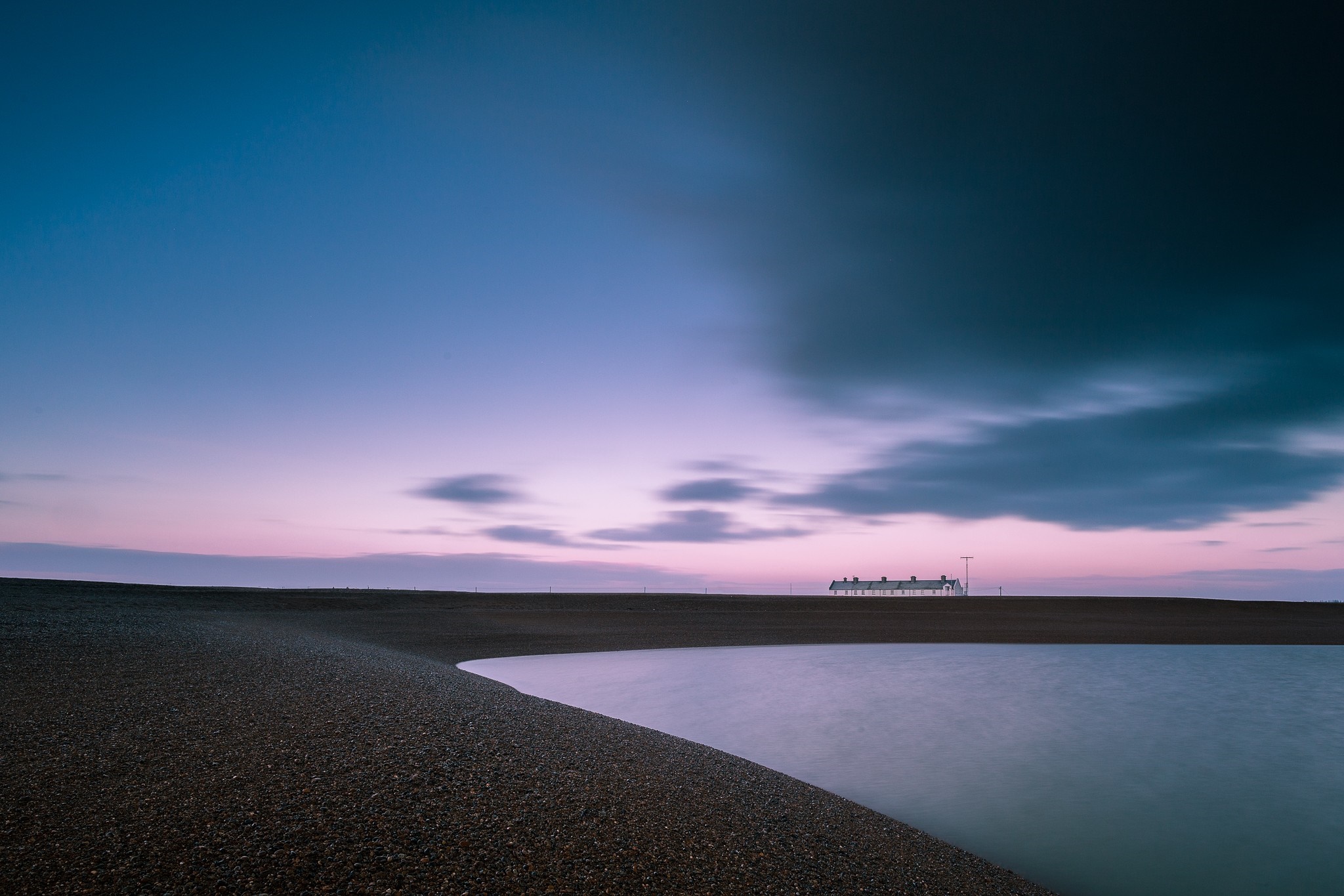Long exposure of a beach at dusk with houses on the horizon HD Wallpaper