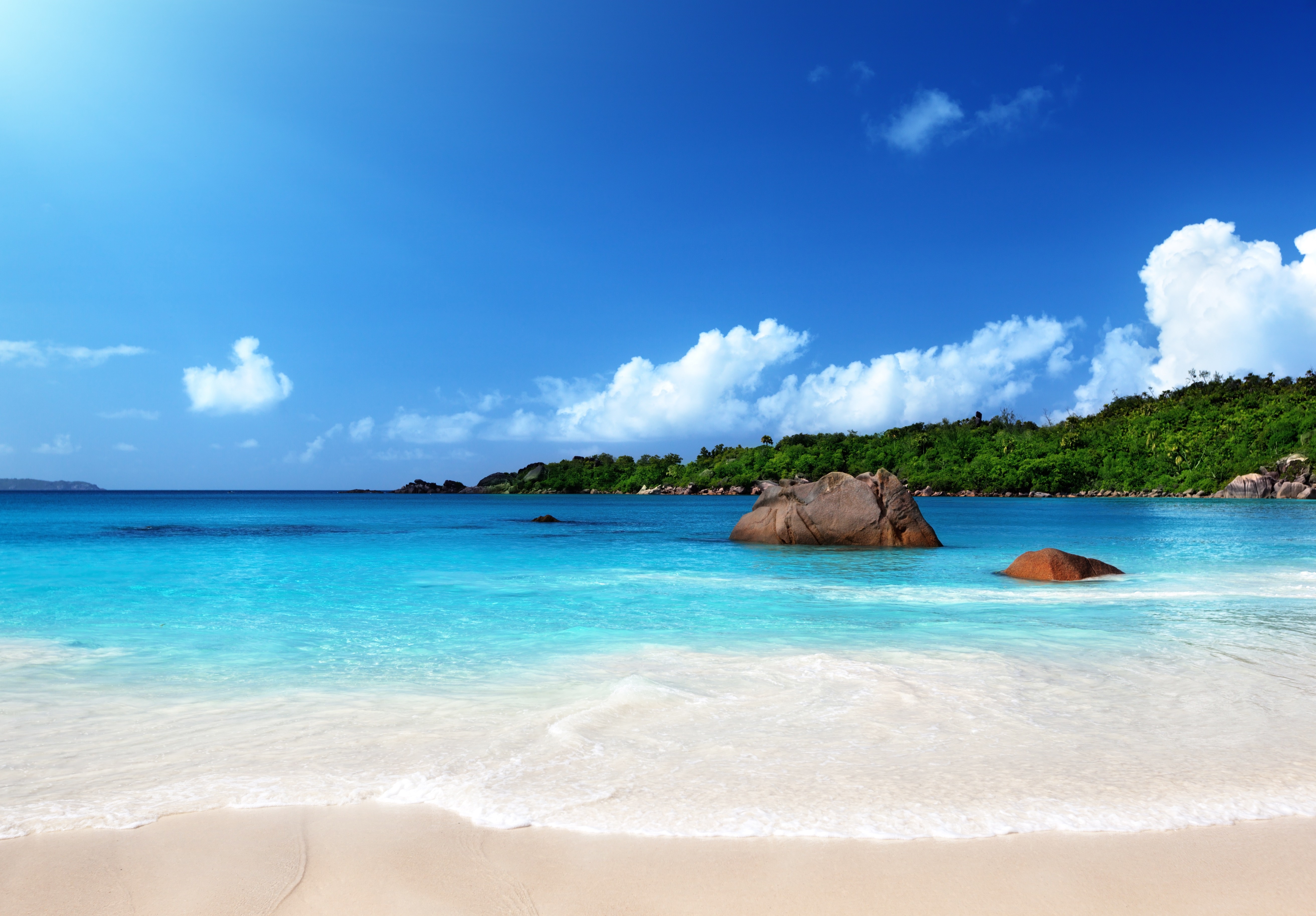 Turquoise ocean waves lap onto a sandy beach with large rocks HD Wallpaper