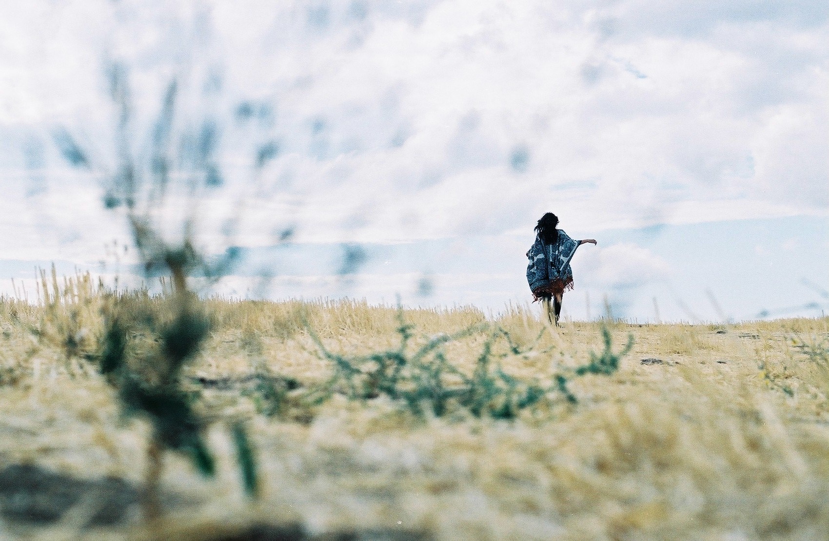 Woman in poncho walking in a dry grassy landscape HD Wallpaper