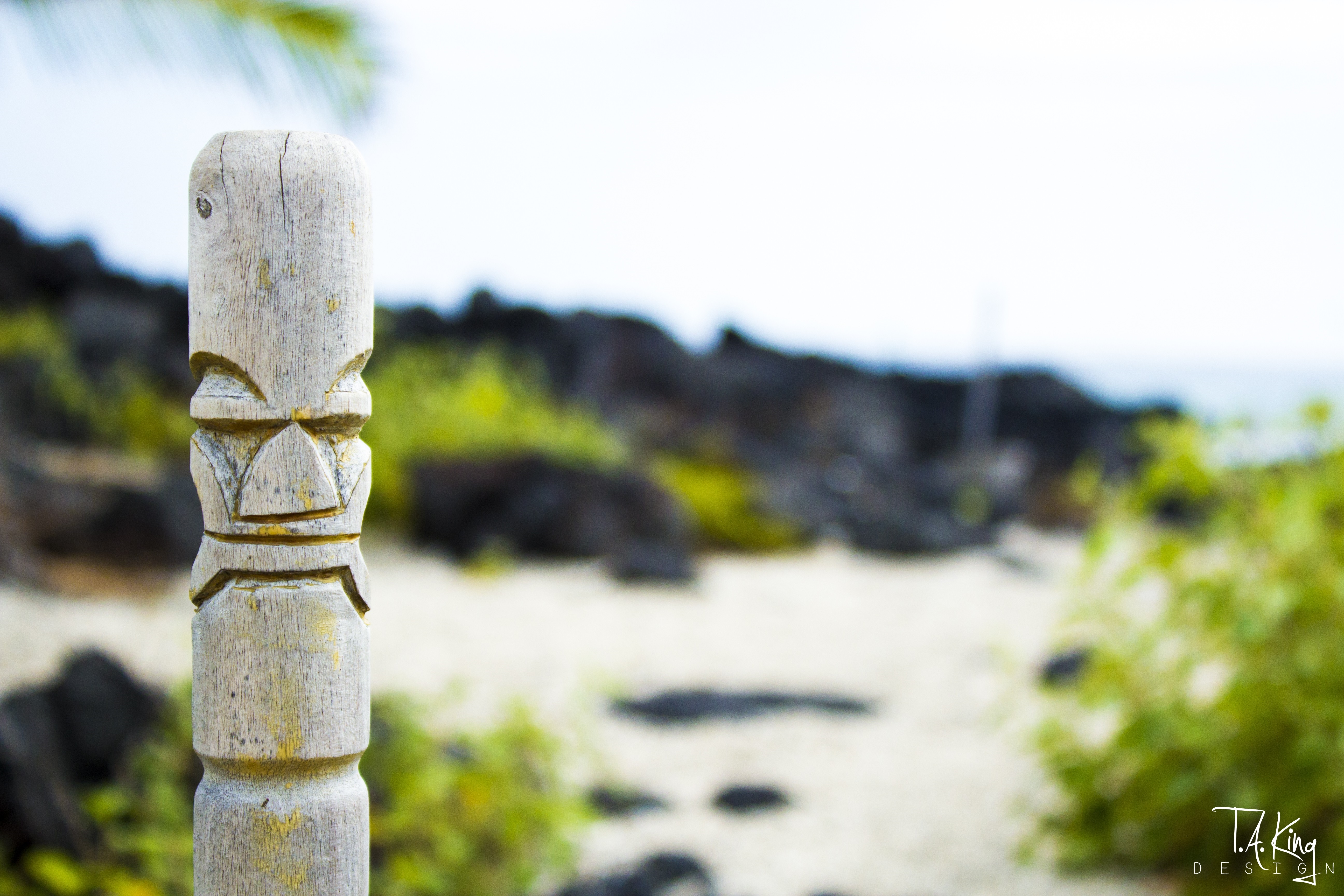 Wooden Tiki statue on a beach with lava rocks HD Wallpaper