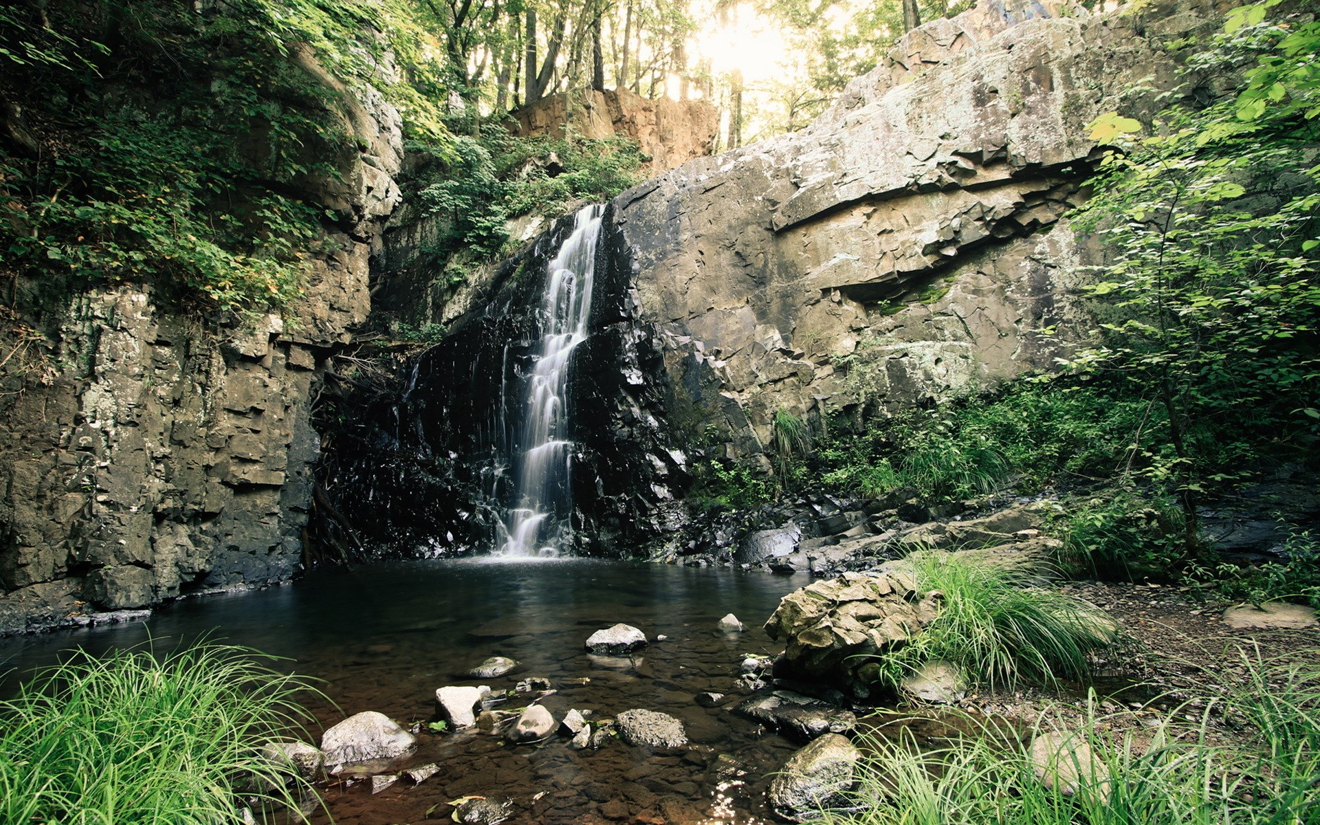 Waterfall cascading into a pool in a rocky forest HD Wallpaper