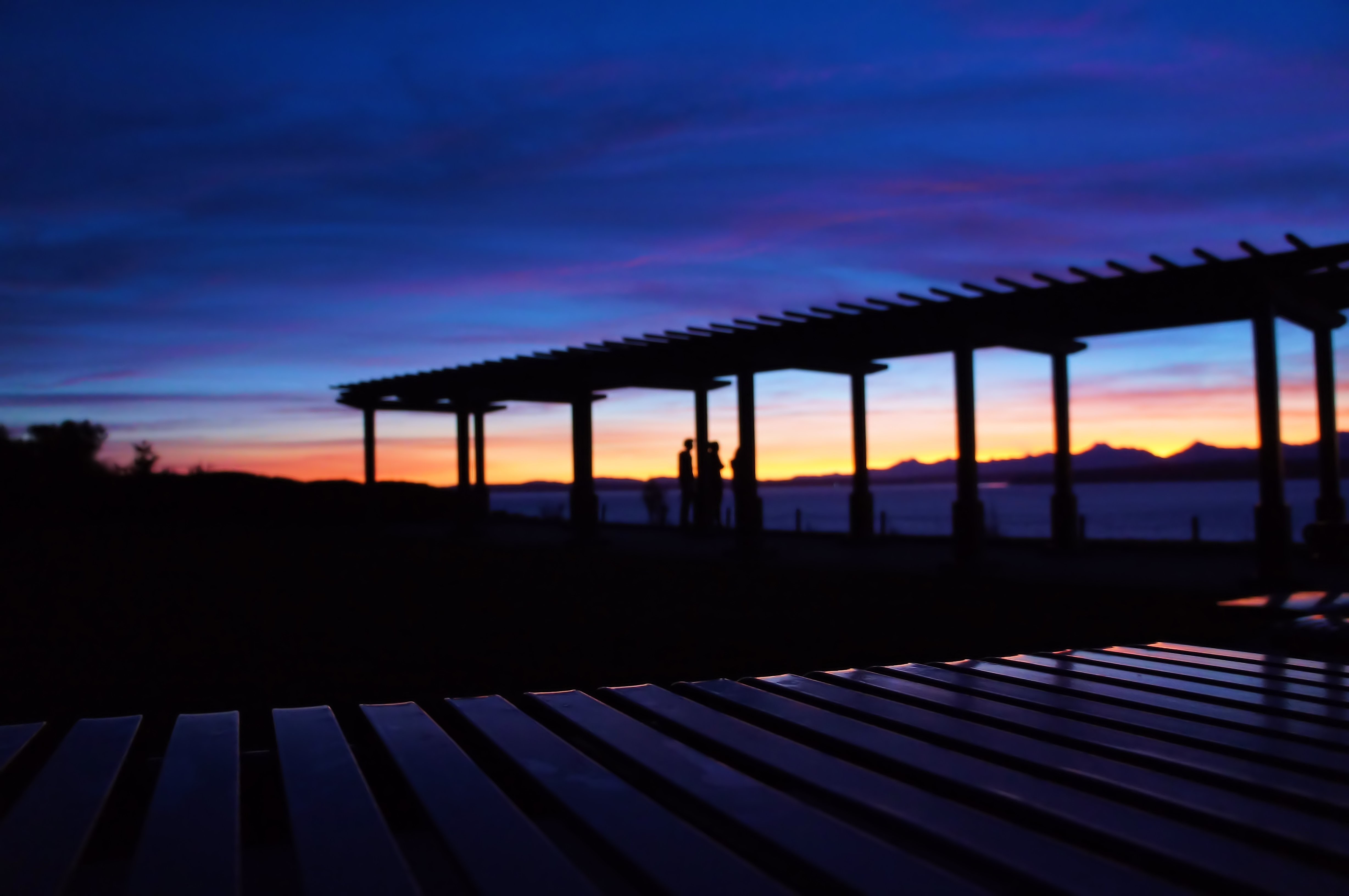 Silhouettes under a pergola at sunset over the water HD Wallpaper