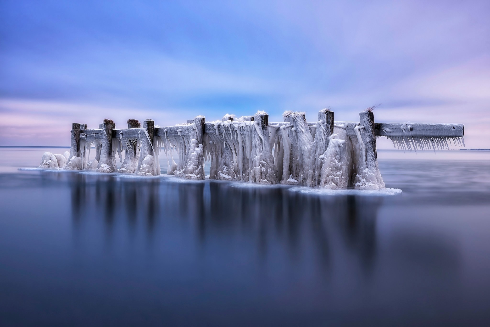 Frozen pier with icicles over calm water at dawn HD Wallpaper