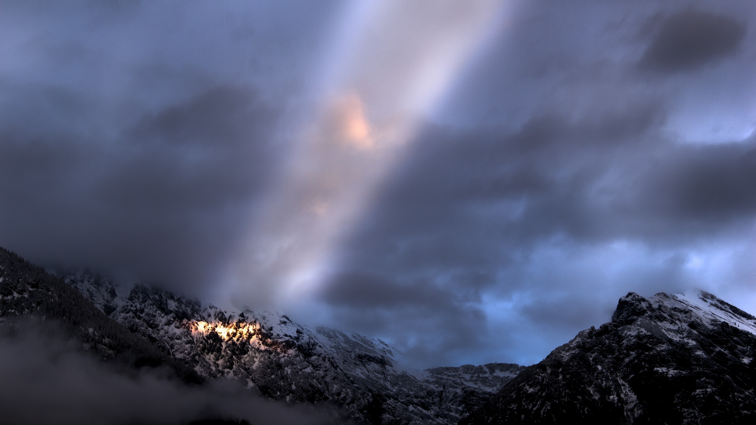 Sunbeam illuminates snowy mountains under cloudy sky HD Wallpaper