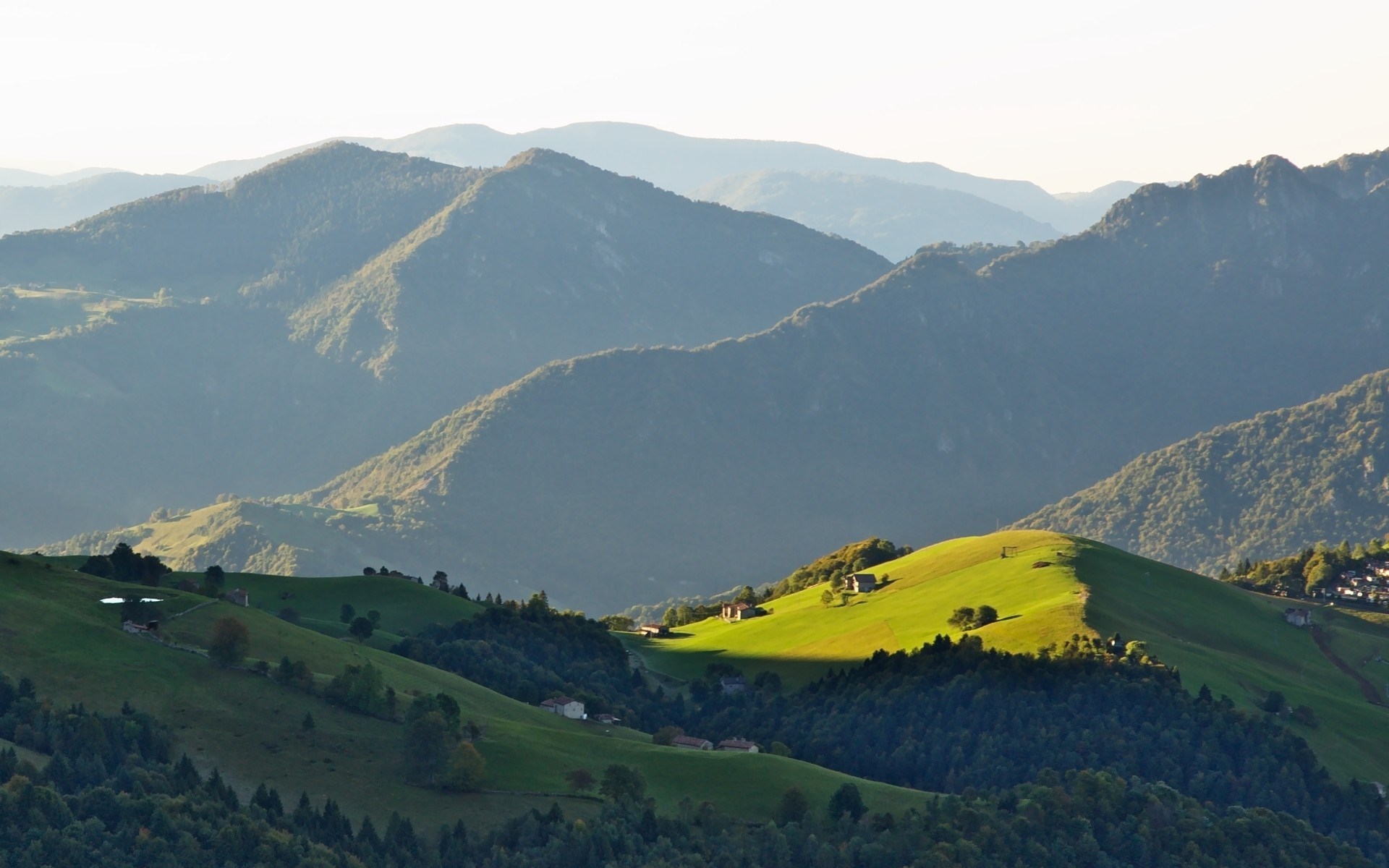 Rolling green hills and mountains under a clear sky HD Wallpaper