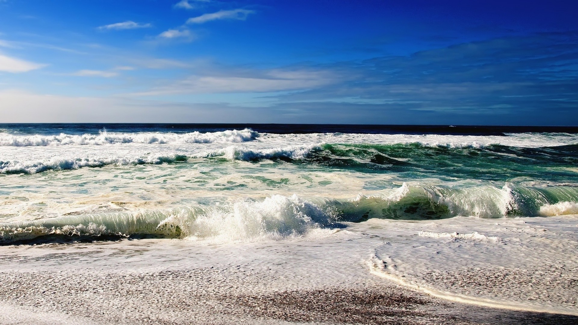 Ocean waves crashing on a sandy beach under a blue sky HD Wallpaper