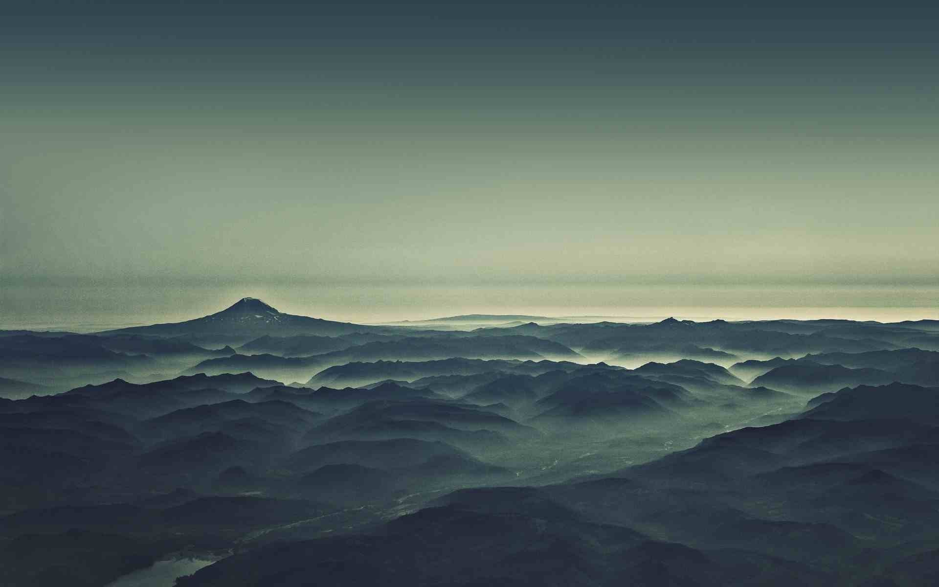 Misty mountain range with a prominent peak on the horizon HD Wallpaper