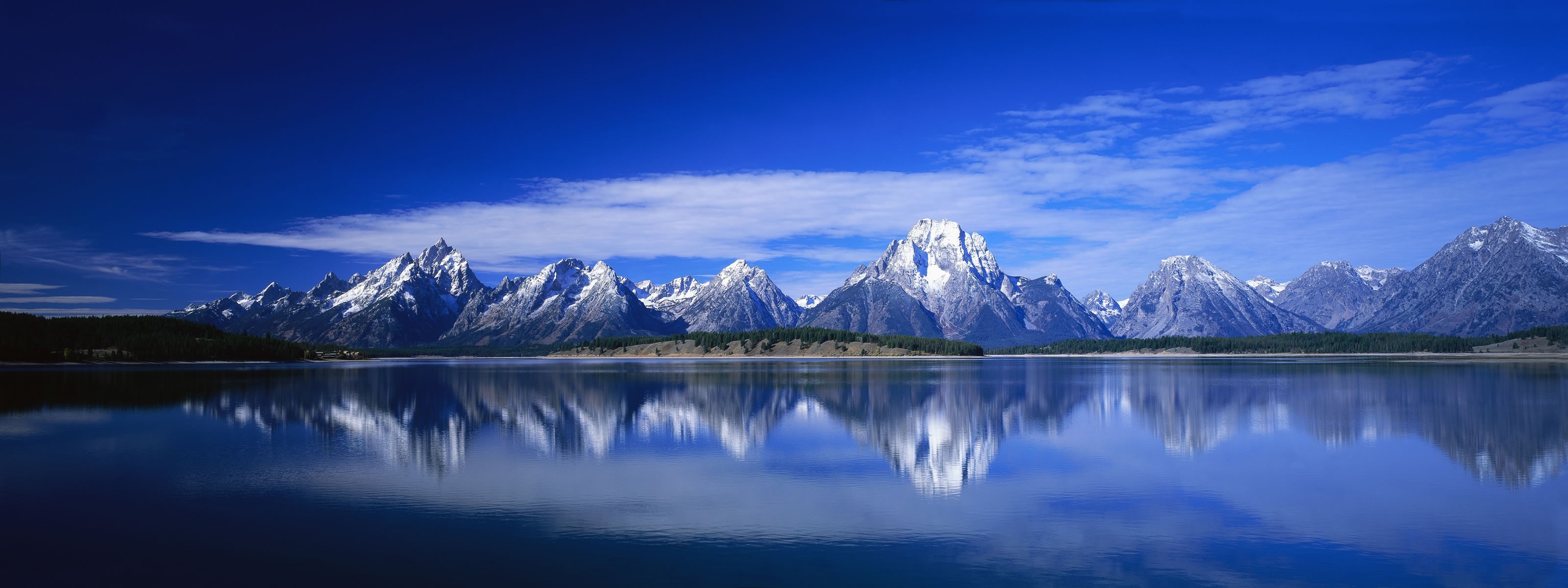 Snow-capped mountains reflected in a calm lake under a blue sky HD Wallpaper