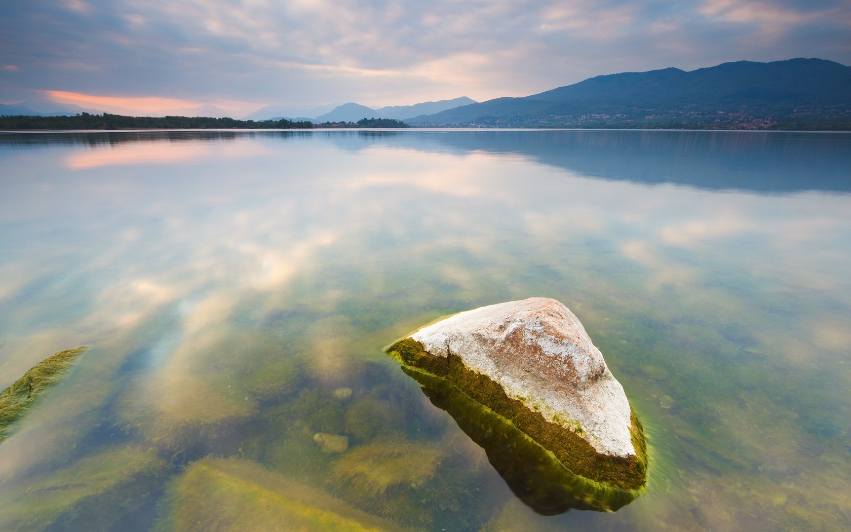 Rock in a calm lake with mountains and clouds at sunset HD Wallpaper