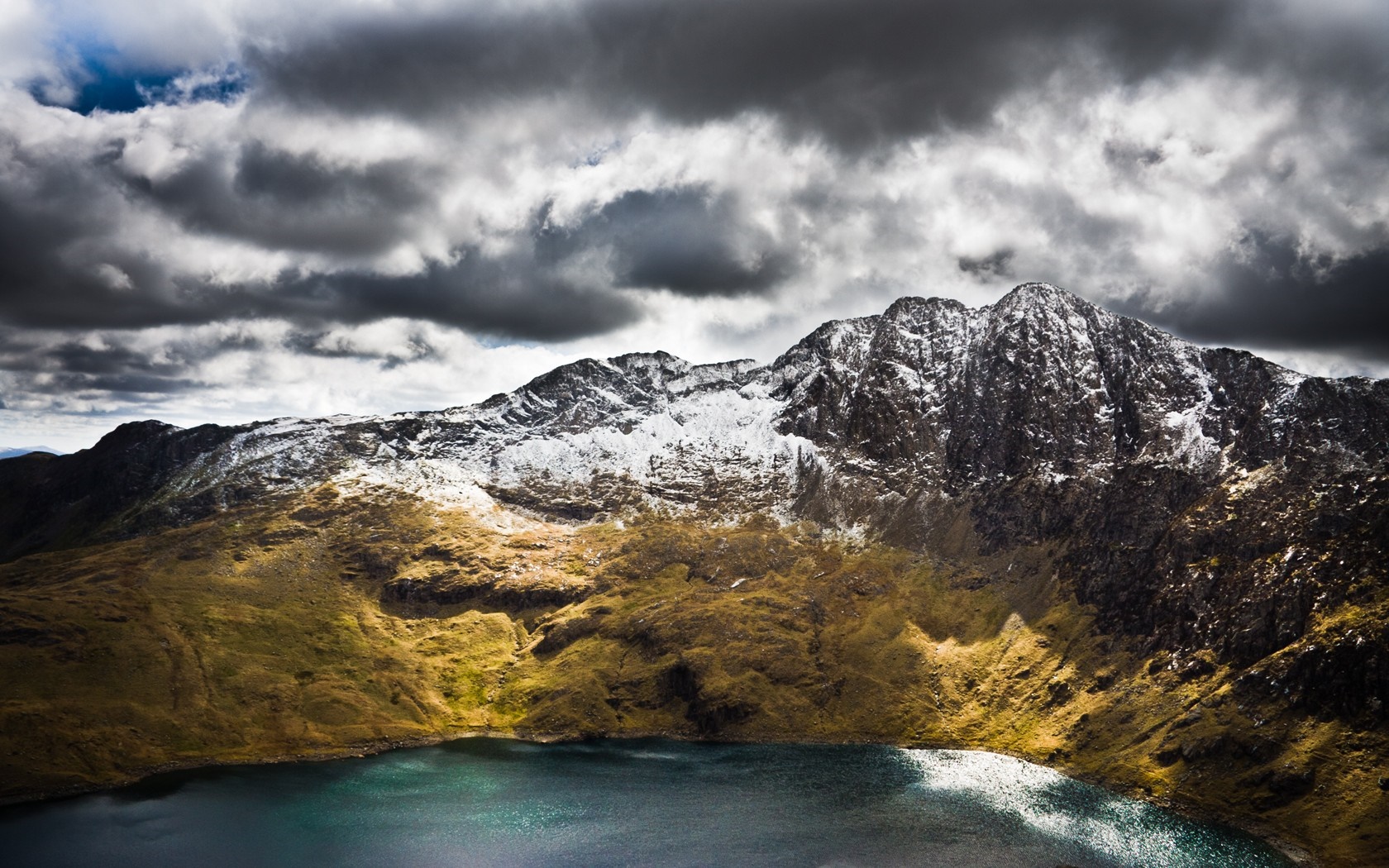 Snow-capped mountain range overlooking a dark lake under stormy clouds HD Wallpaper