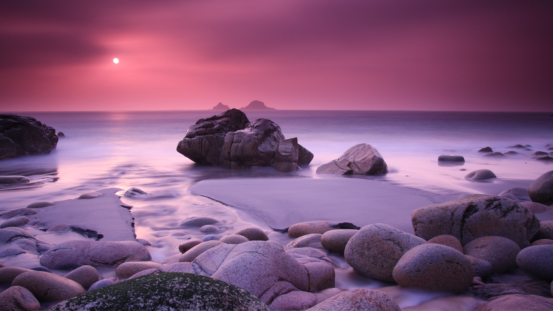 Purple sunset over a rocky beach with calm ocean waves HD Wallpaper