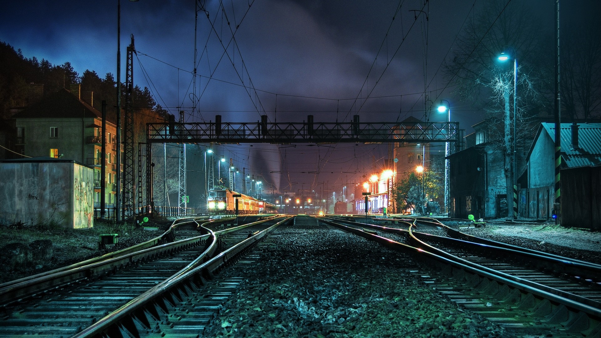 Train station at night with multiple tracks and overhead wires HD Wallpaper