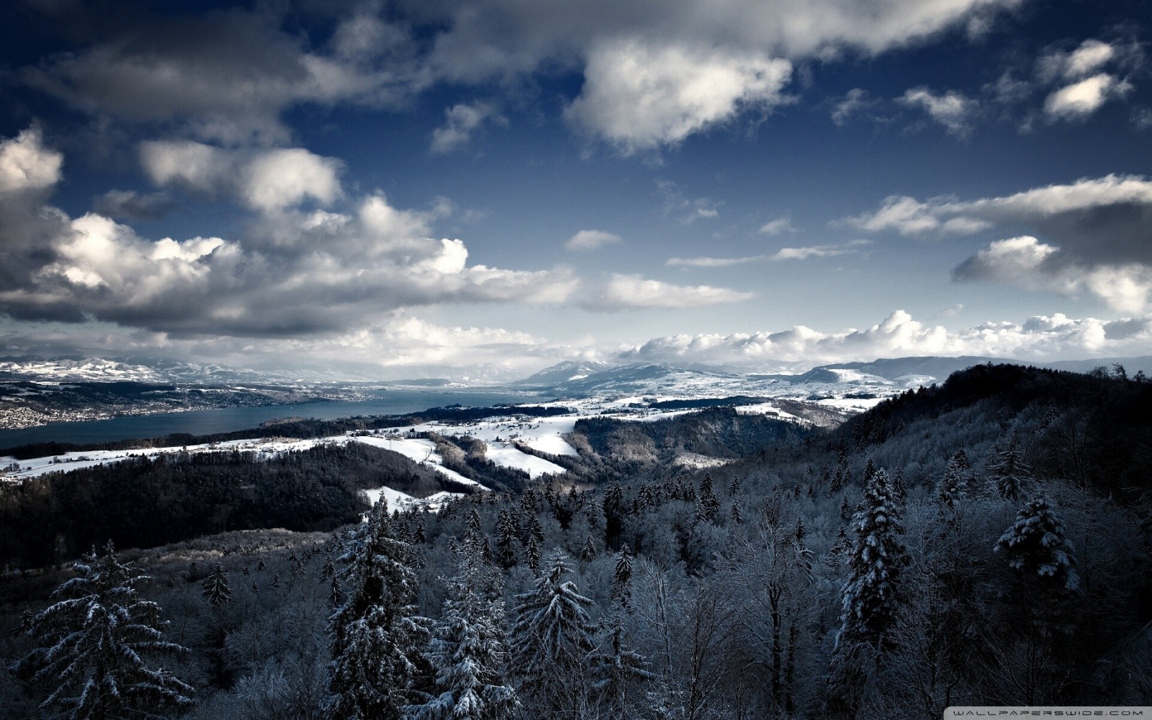 Winter landscape with snow-covered mountains and a lake under a cloudy sky HD Wallpaper
