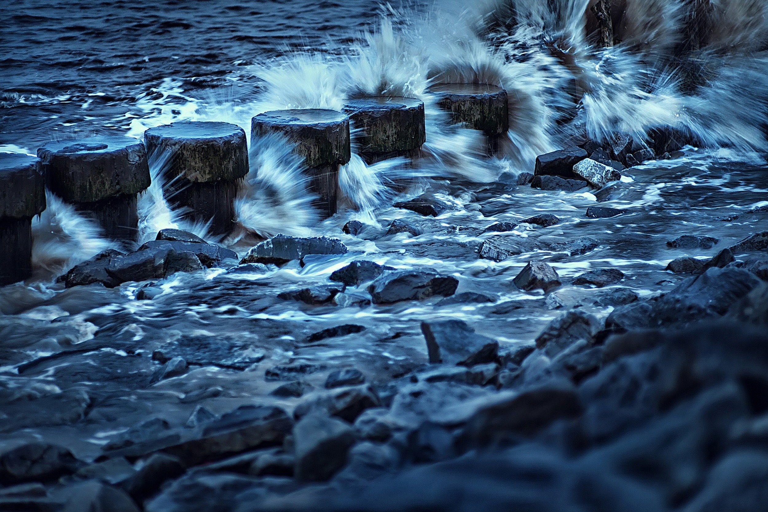 Waves crashing on wooden posts and rocks HD Wallpaper