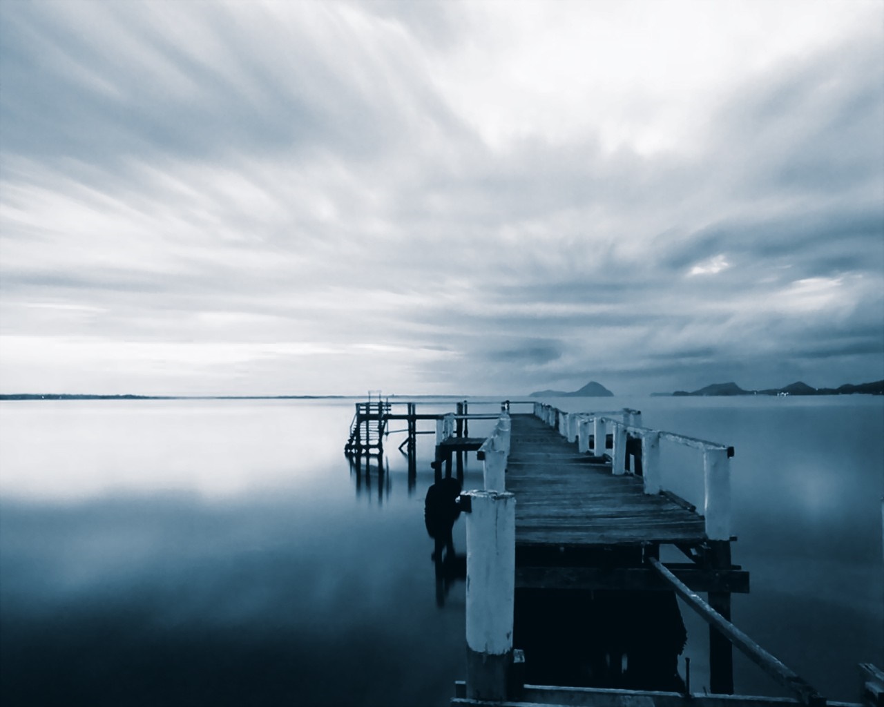 Wooden pier extending into a calm body of water under a cloudy sky HD Wallpaper