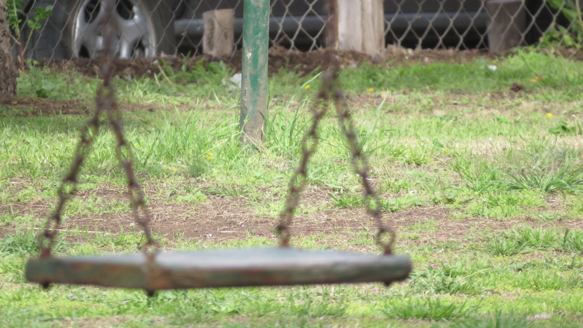 Rusty swing set chains and seat in a grassy yard HD Wallpaper