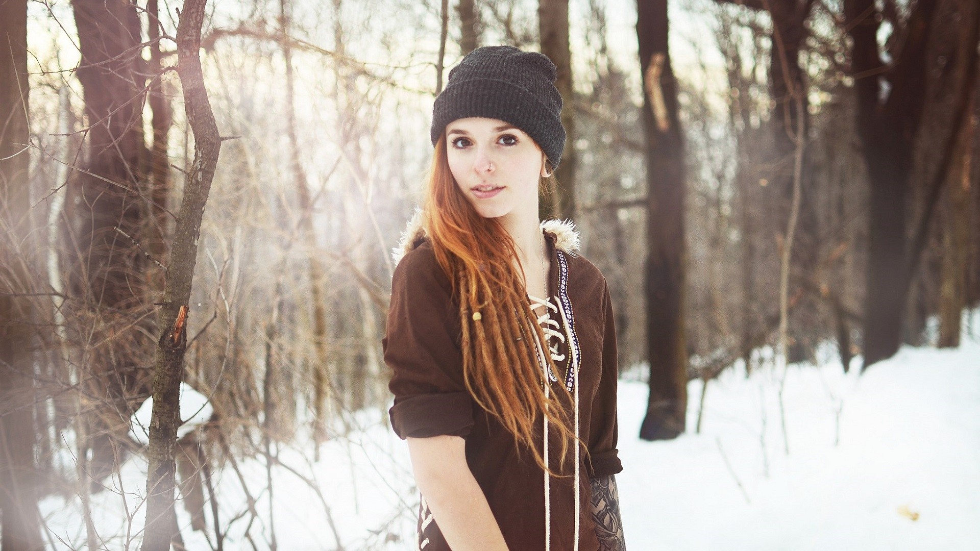 Woman with dreadlocks wearing a beanie in a snowy forest HD Wallpaper