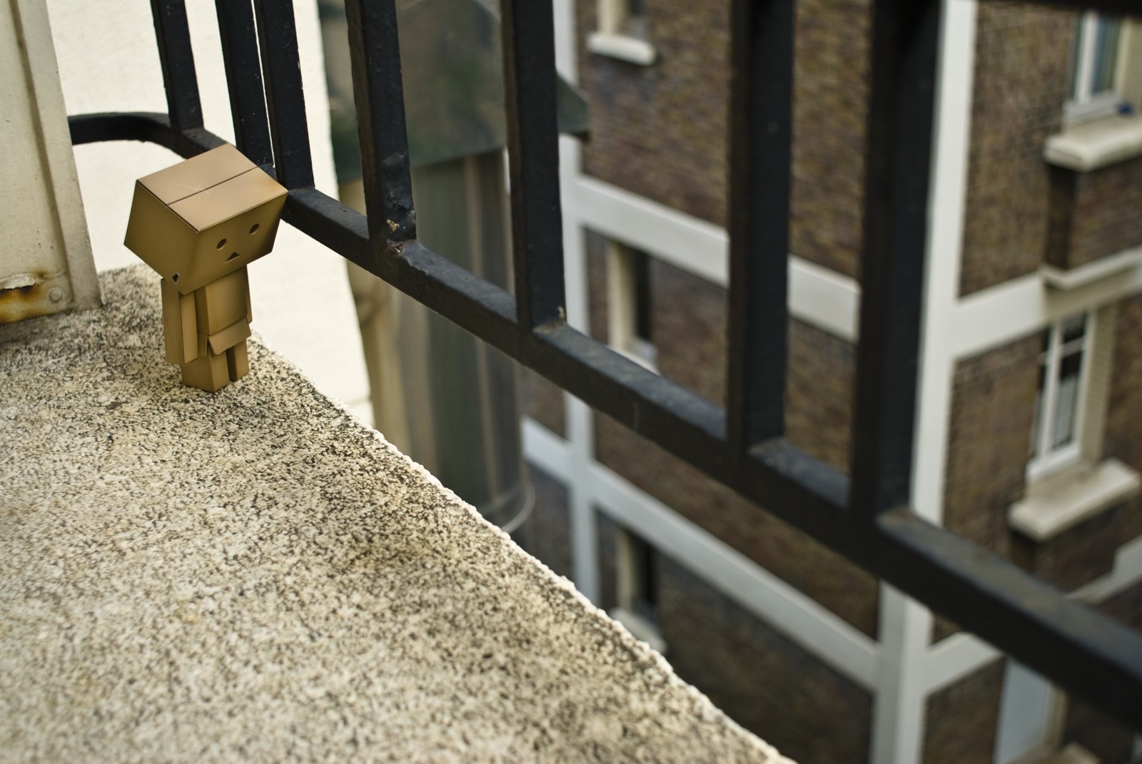 Danbo toy on a balcony railing overlooking a building HD Wallpaper
