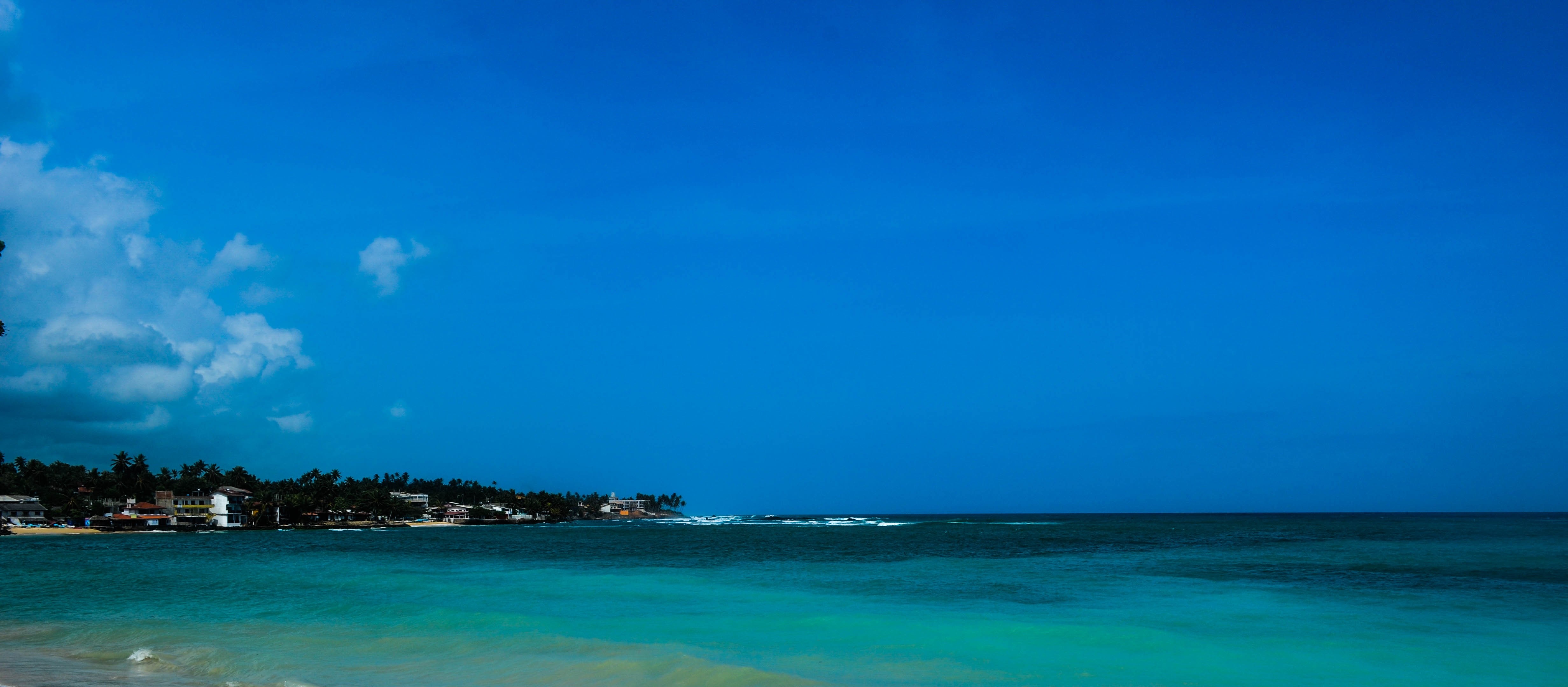 Turquoise ocean with a distant coastline under a bright blue sky HD Wallpaper