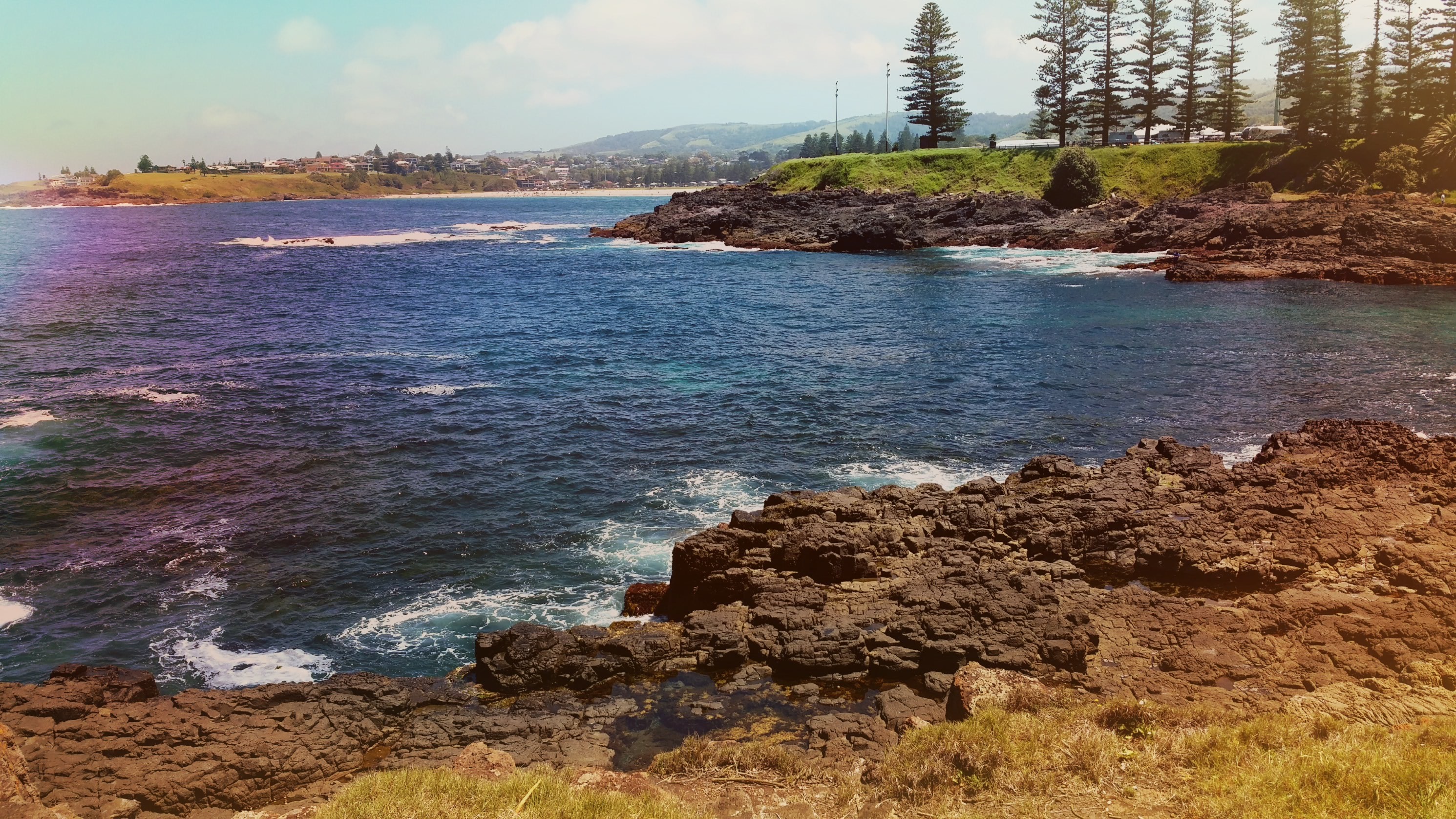 Rocky coastline with ocean and distant town HD Wallpaper