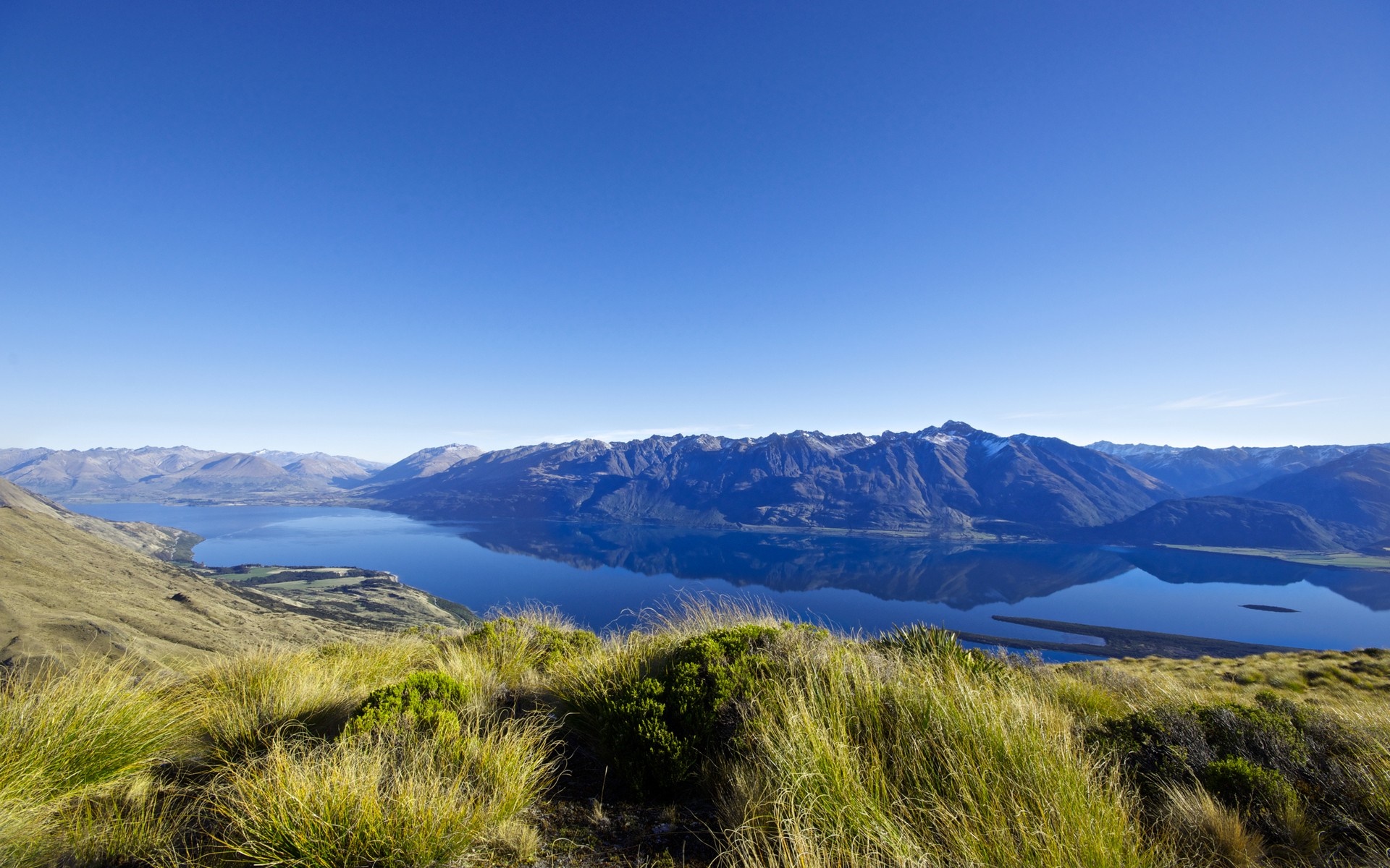 Mountain range reflected in a calm lake with grassy foreground HD Wallpaper