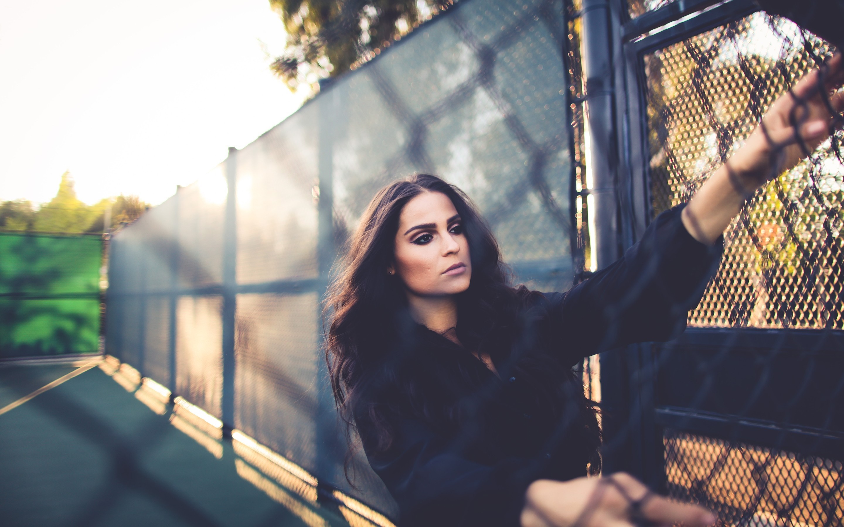 Woman leaning on a chain-link fence at sunset HD Wallpaper