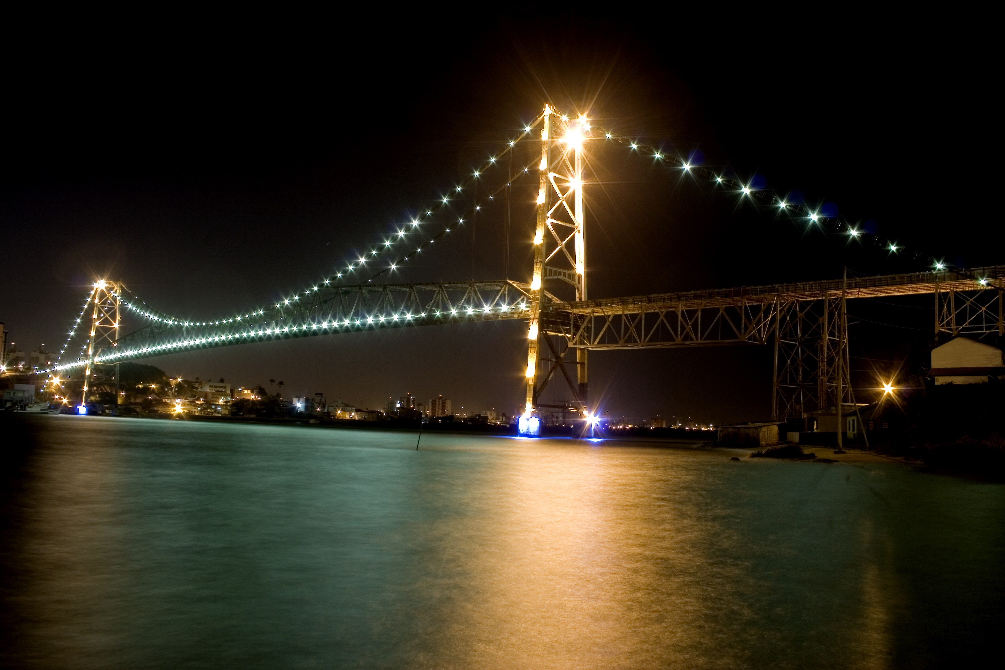 Illuminated suspension bridge over water at night HD Wallpaper
