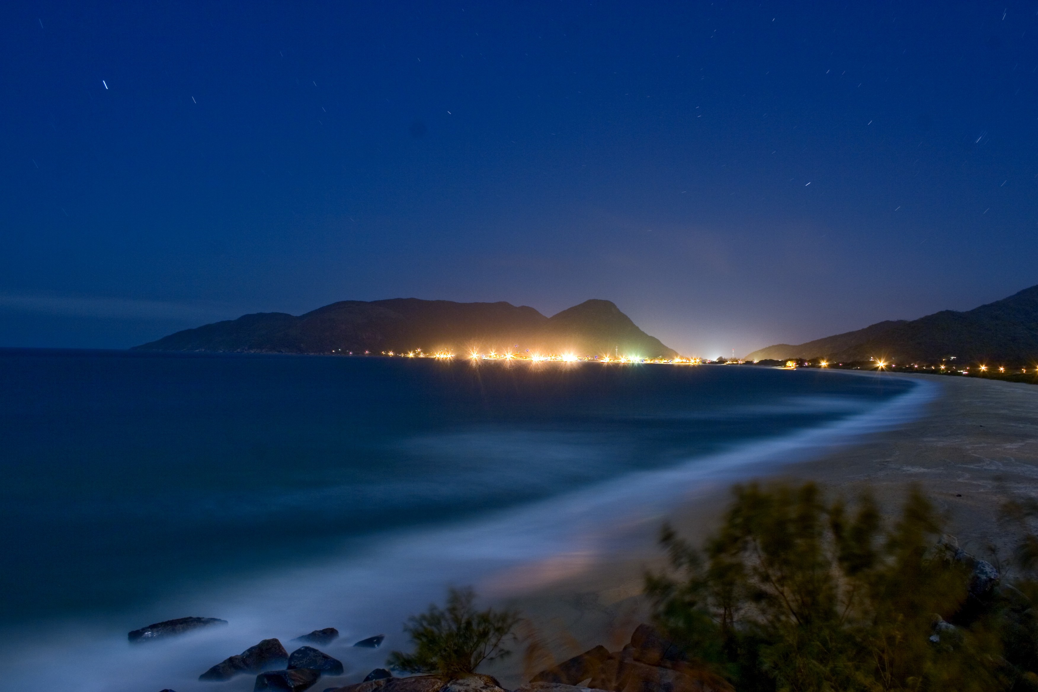 Coastal town lights at night with ocean and mountains HD Wallpaper