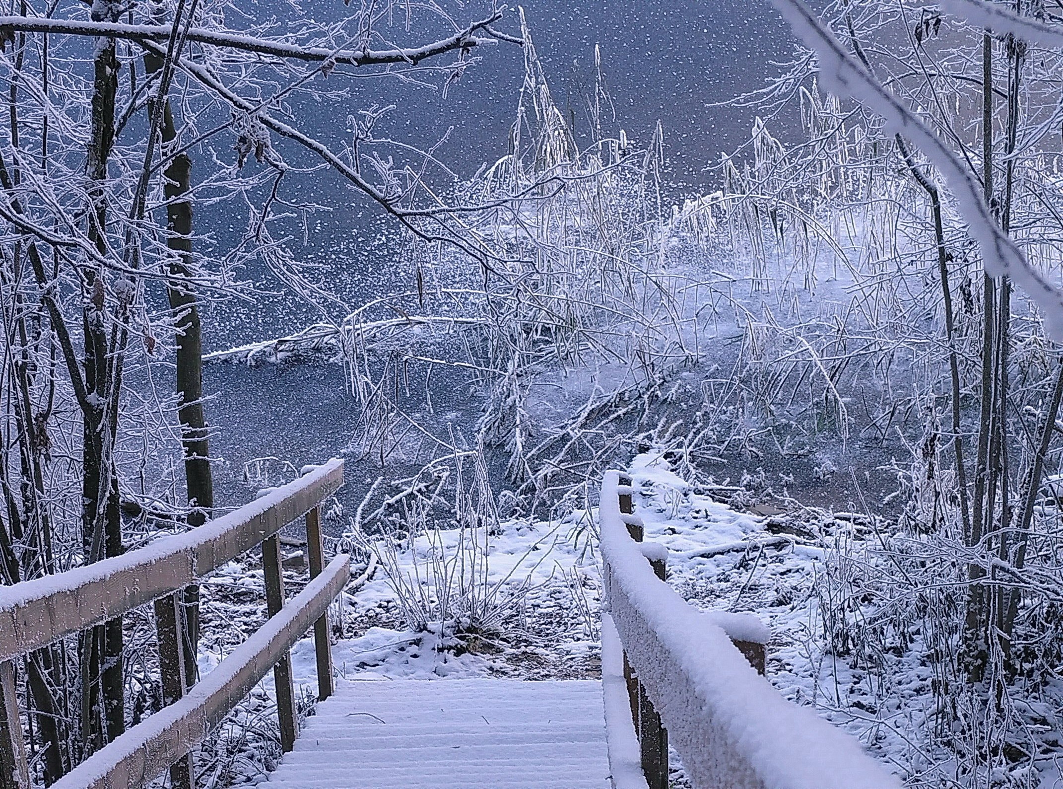 Snow-covered wooden stairs leading to a frozen lake in winter HD Wallpaper