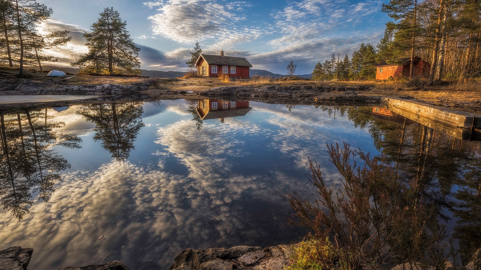 Red cabin reflected in a calm lake with trees and sky HD Wallpaper